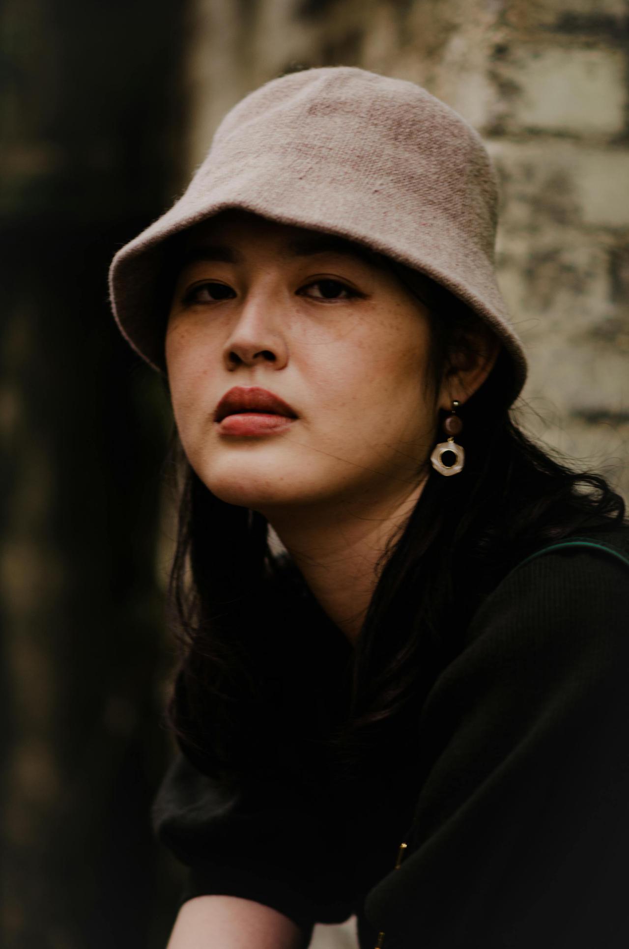 Close-up portrait of a young woman in a bucket hat, captured outdoors with a warm tone.
