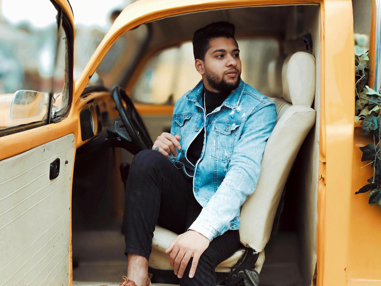 Young man sitting in a yellow vintage car, enjoying a relaxed moment outdoors.