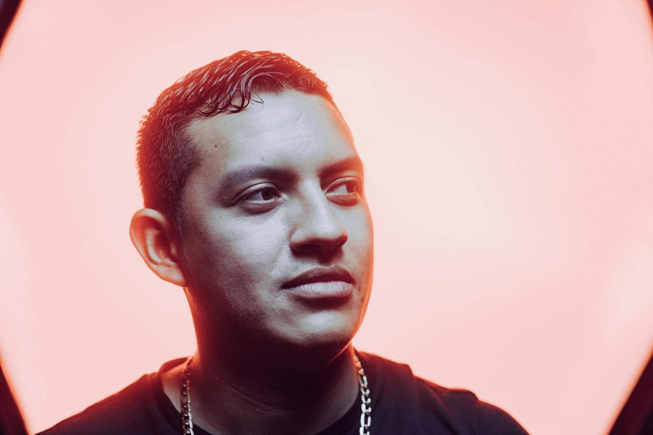 Close-up portrait of a young man with a stylish necklace against a pink background, emphasizing modern fashion.