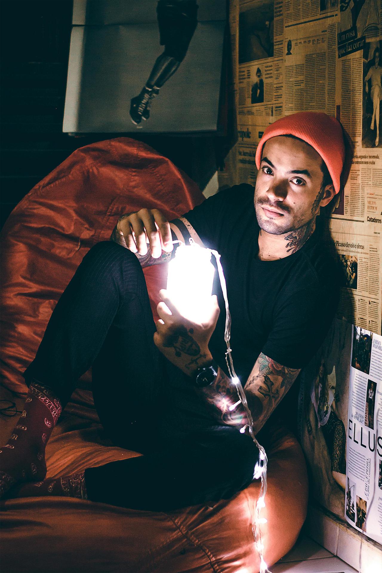 A fashionable young man sitting with glowing string lights, creating a moody indoor portrait.