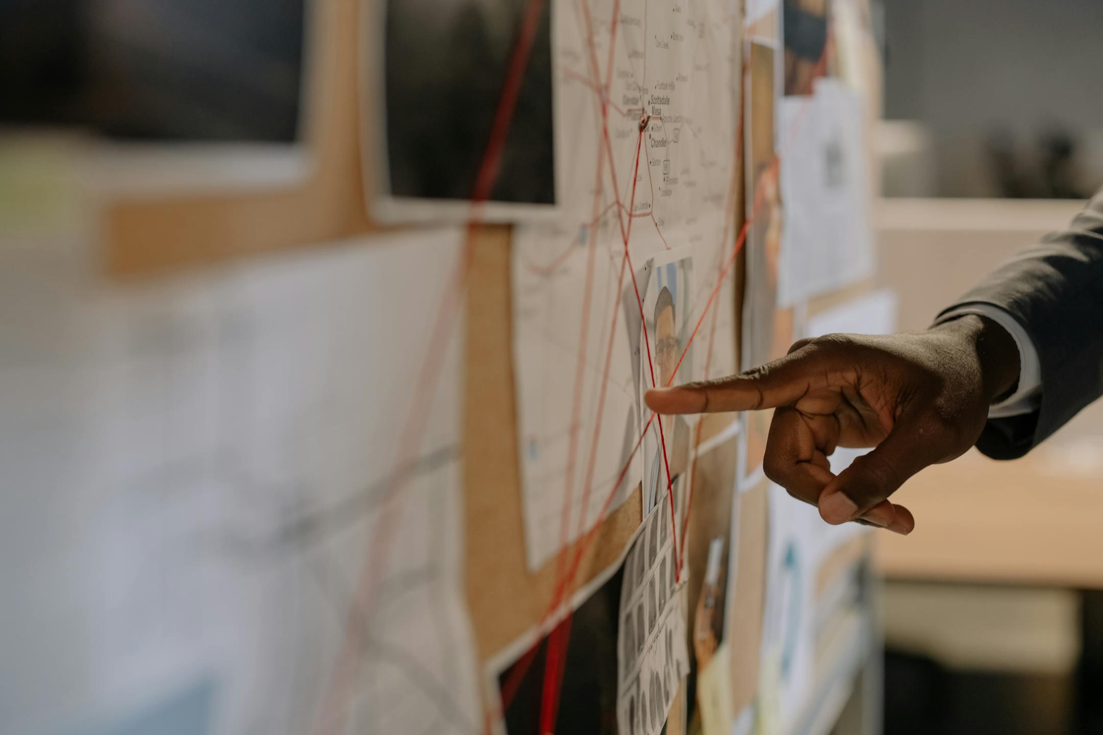 Close-up of an investigator pointing at an evidence board with connected clues using red strings.