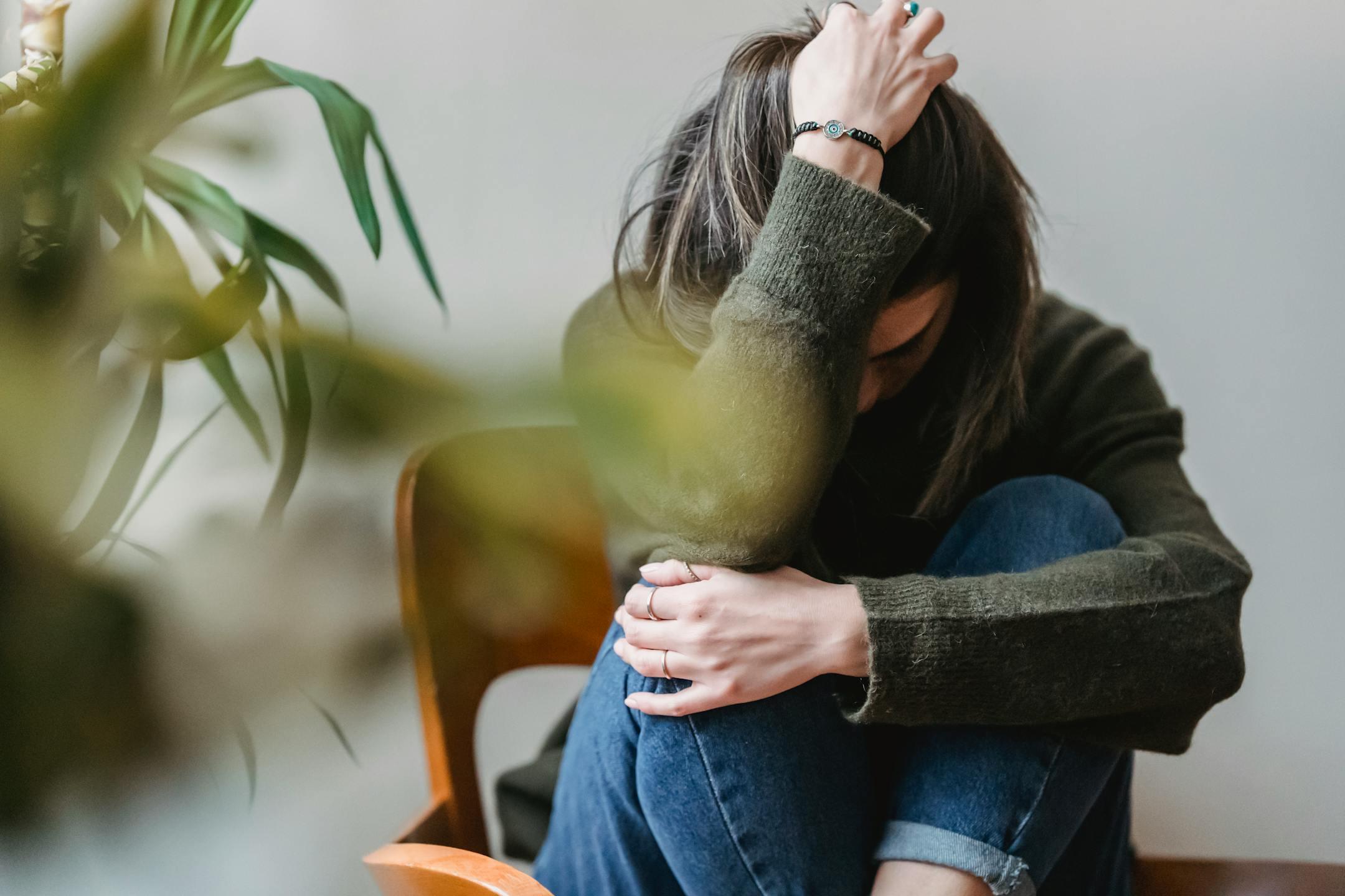 Anonymous young woman sitting at home, touching her hair and embracing her knees, depicting anxiety and emotional distress supported through Cognitive Analytica’s therapy in Lebanon