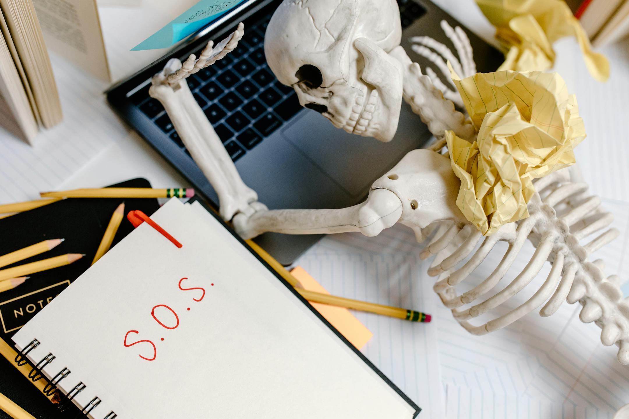 Humorous depiction of office burnout showing a skeleton at a cluttered desk with an S.O.S note, symbolizing workplace stress and exhaustion at Cognitive Analytica Lebanon.