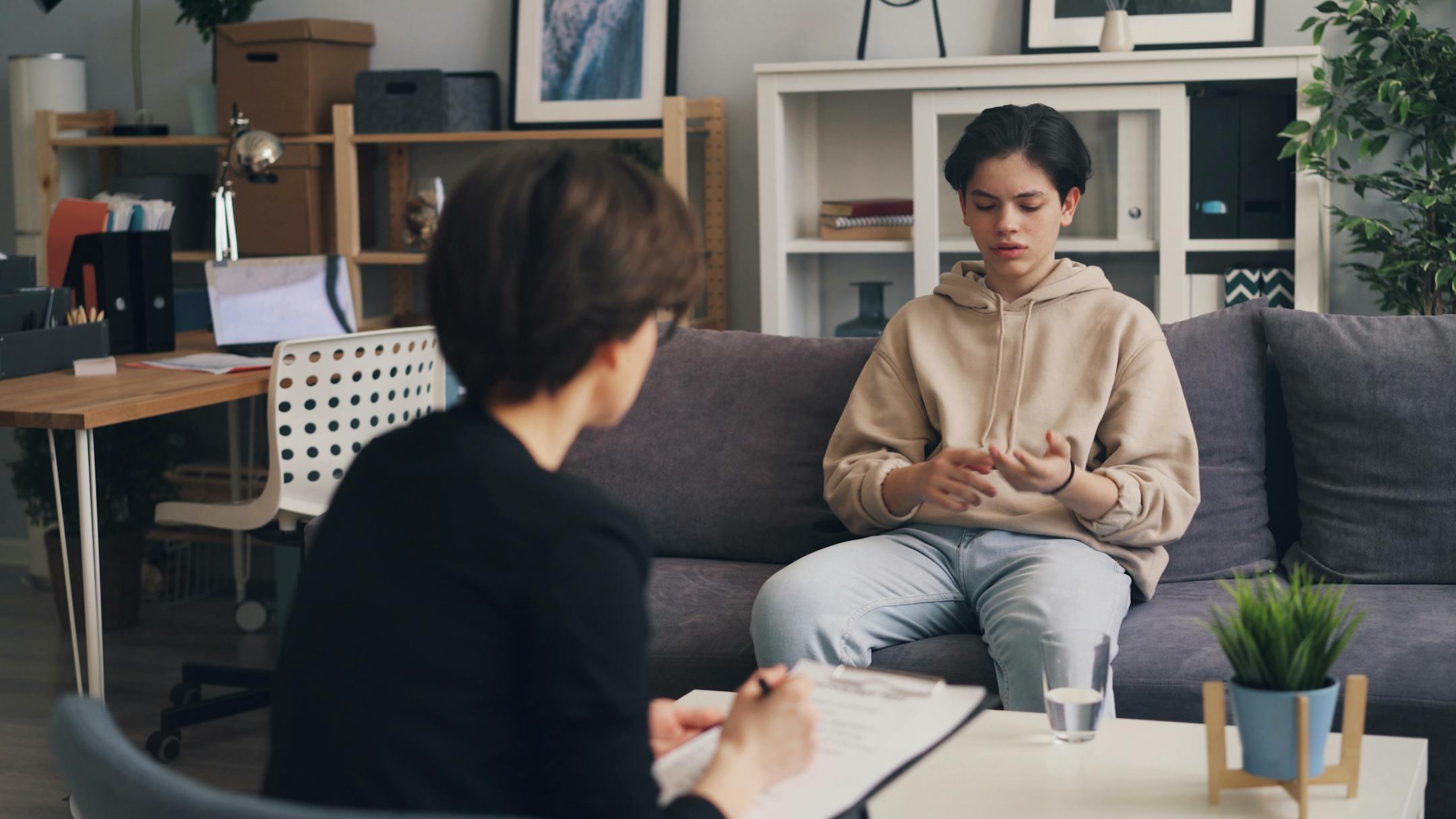 A teenager engages in a therapy session with a professional counselor in a modern office setting.