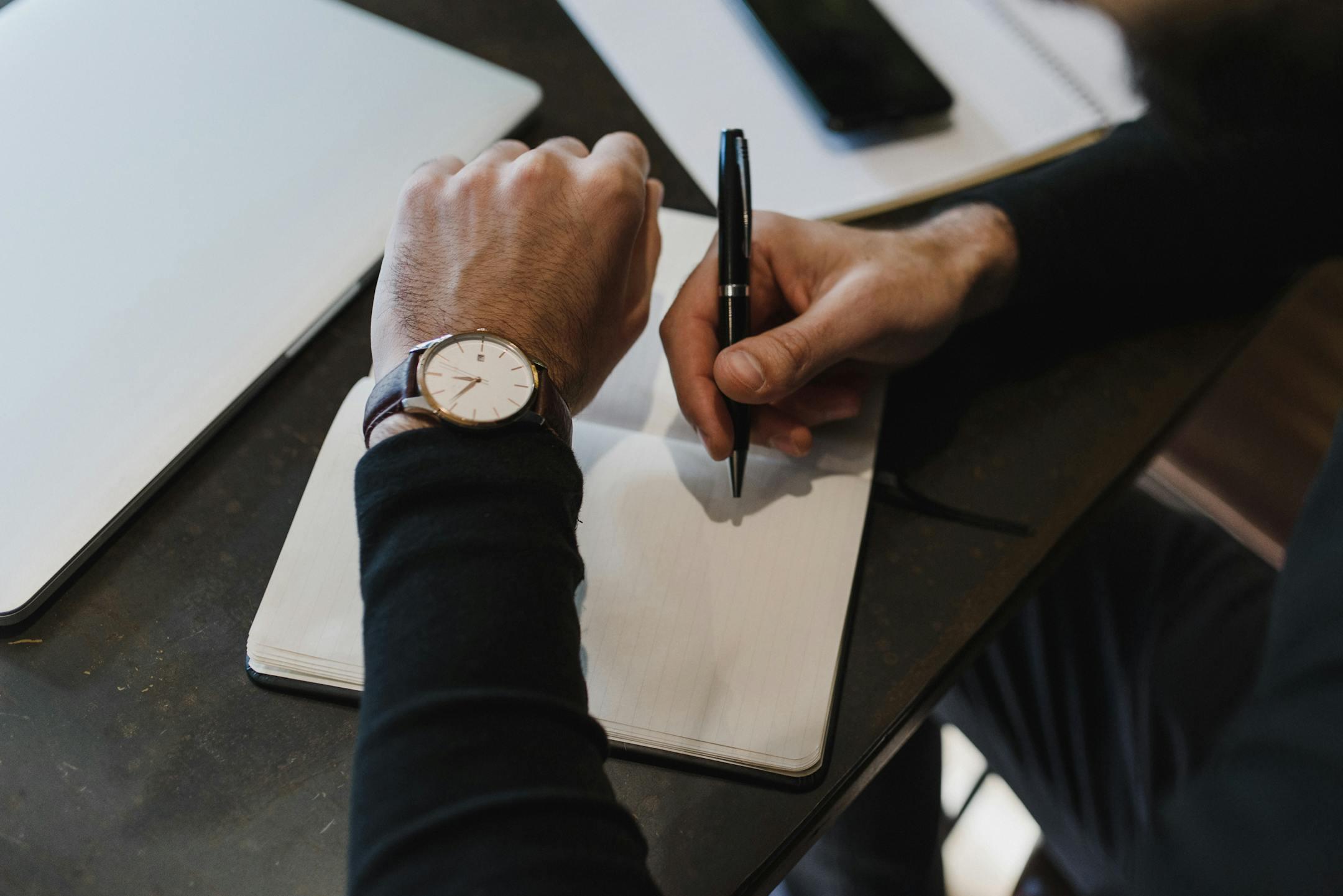 Close-up top view of a person writing in a notebook while preparing to book a therapy session with Cognitive Analytica, symbolizing commitment to mental health and professional care.