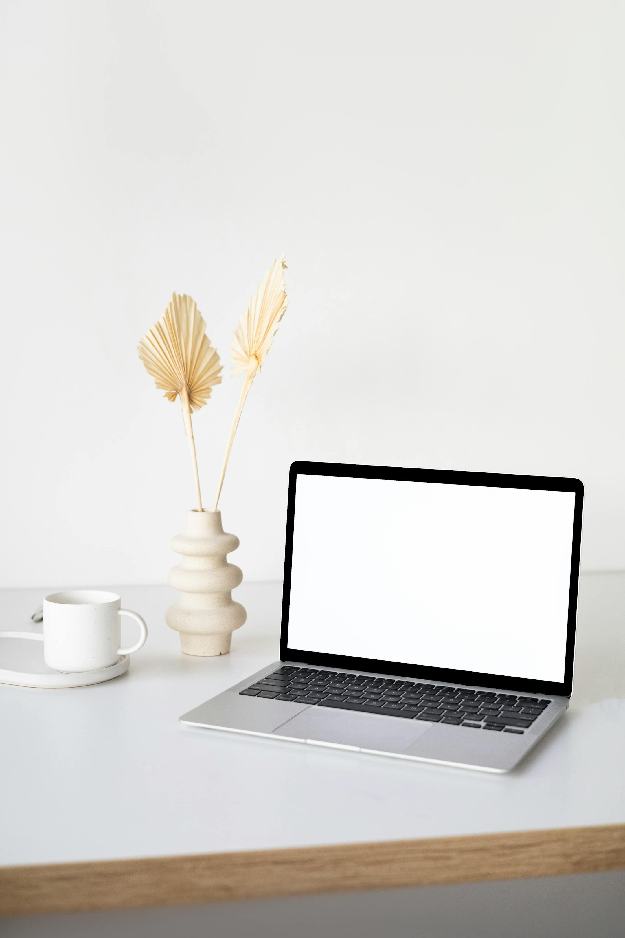 A clean, minimalist workspace featuring a laptop, ceramic vase, and coffee cup on a wooden table — symbolizing comfort, focus, and online therapy with Cognitive Analytica
