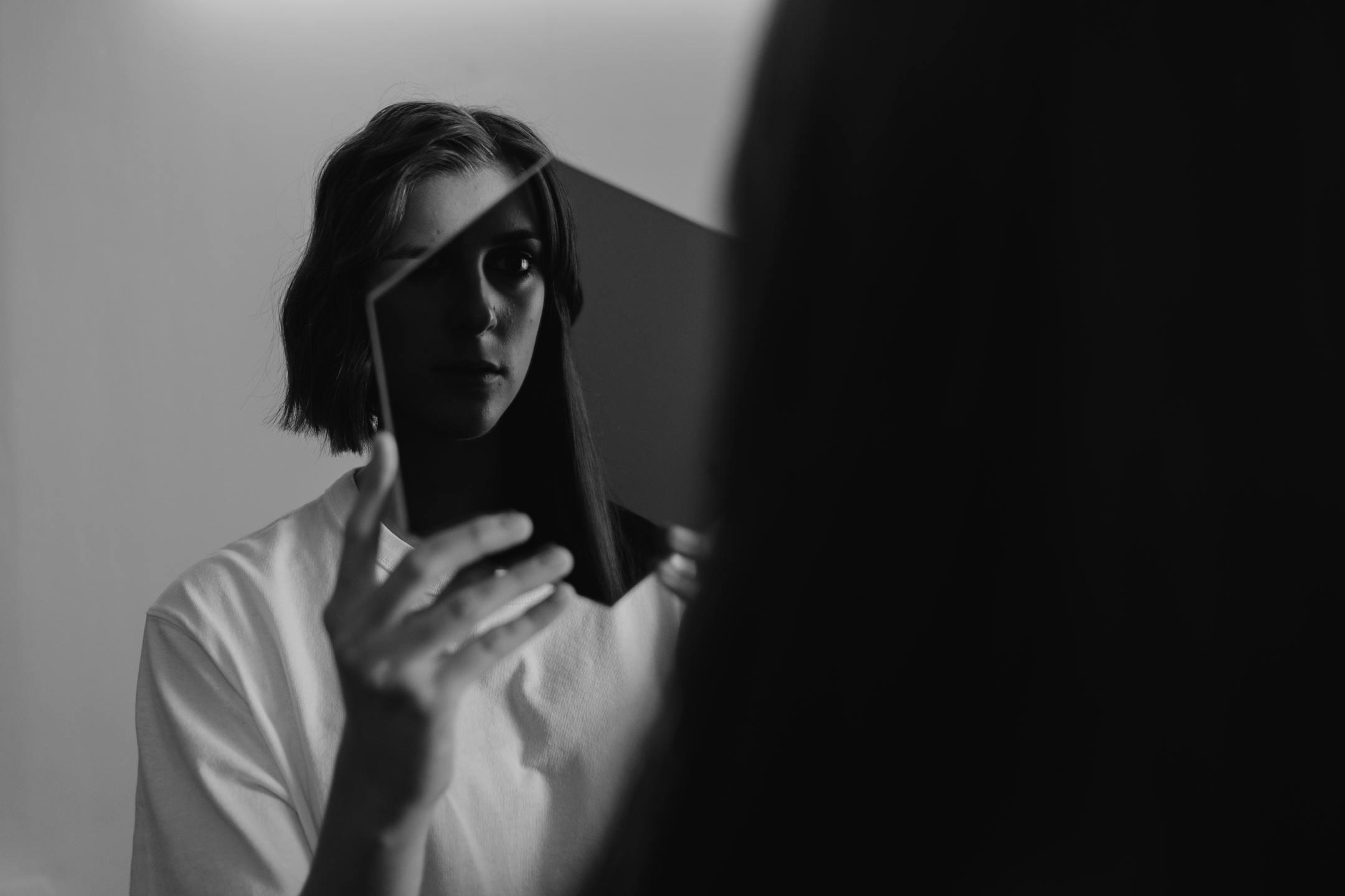 Monochrome image of a woman reflecting on herself in a mirror, evoking introspection, emotional awareness, and vulnerability — Cognitive Analytica, Lebanon<br>