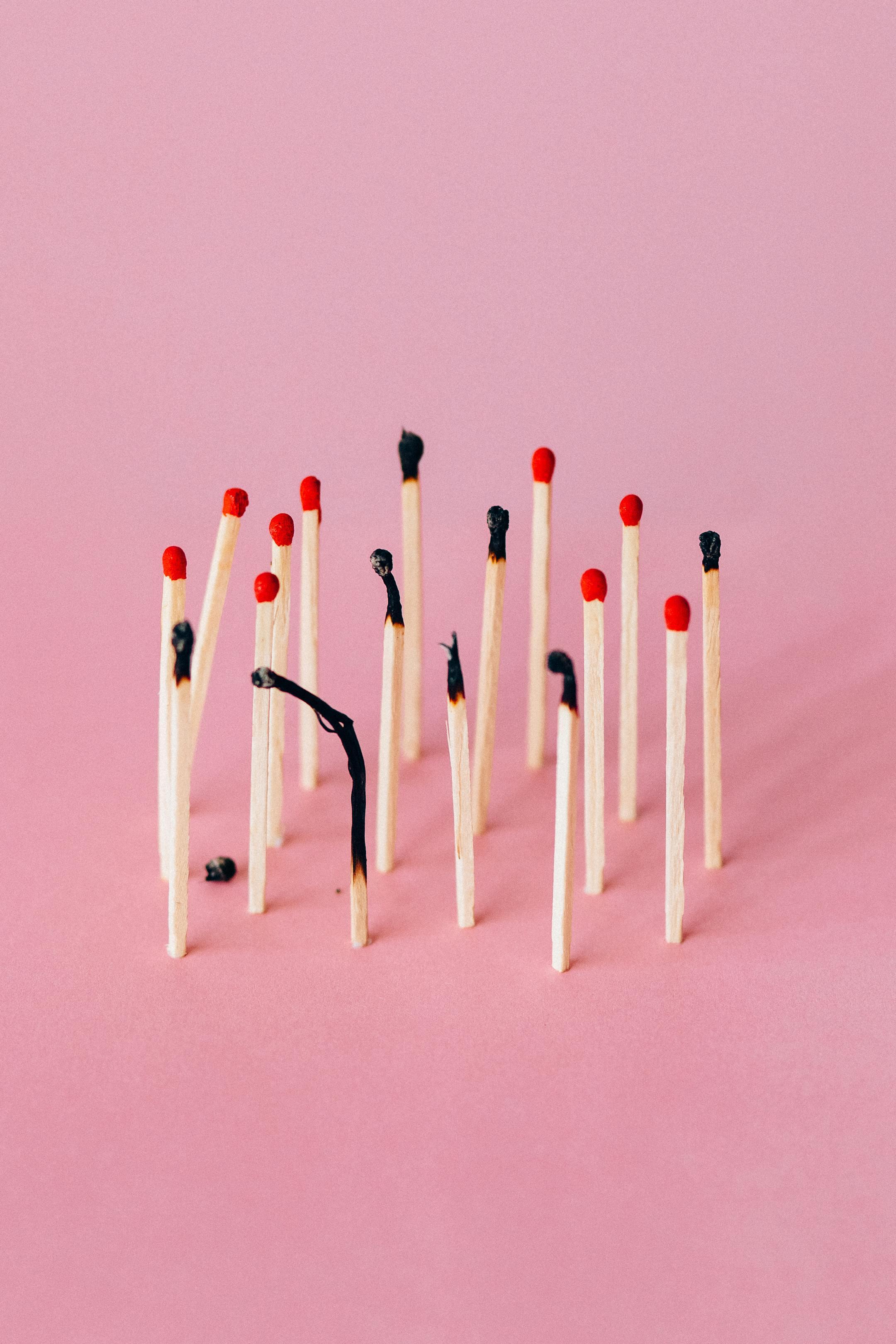 Burned matchsticks arranged on a pink background, symbolizing emotional exhaustion and burnout recovery with Cognitive Analytica Lebanon.