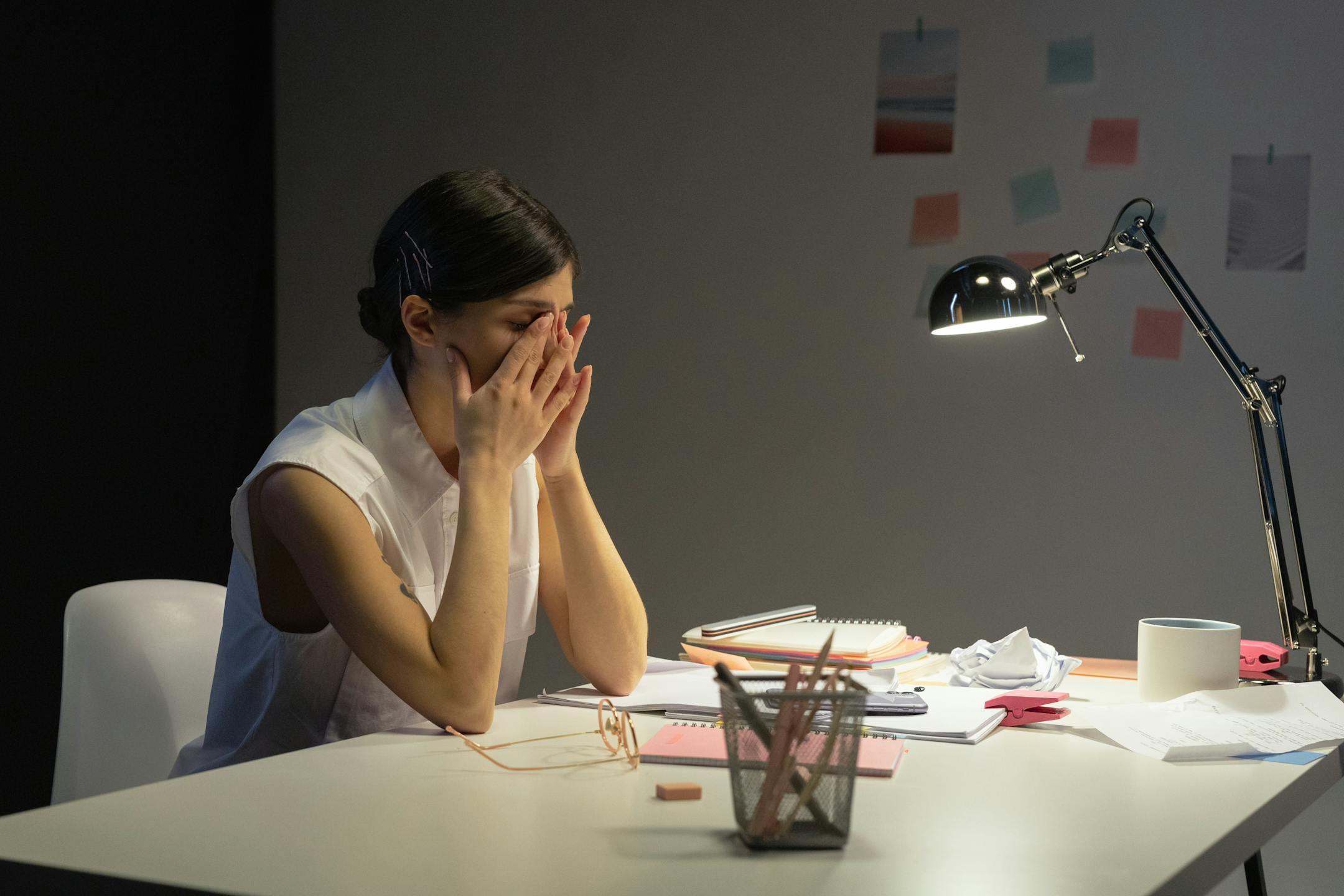 Stressed businesswoman rubbing her eyes at a cluttered desk, illustrating workplace fatigue and emotional exhaustion treated through burnout therapy at Cognitive Analytica Lebanon.