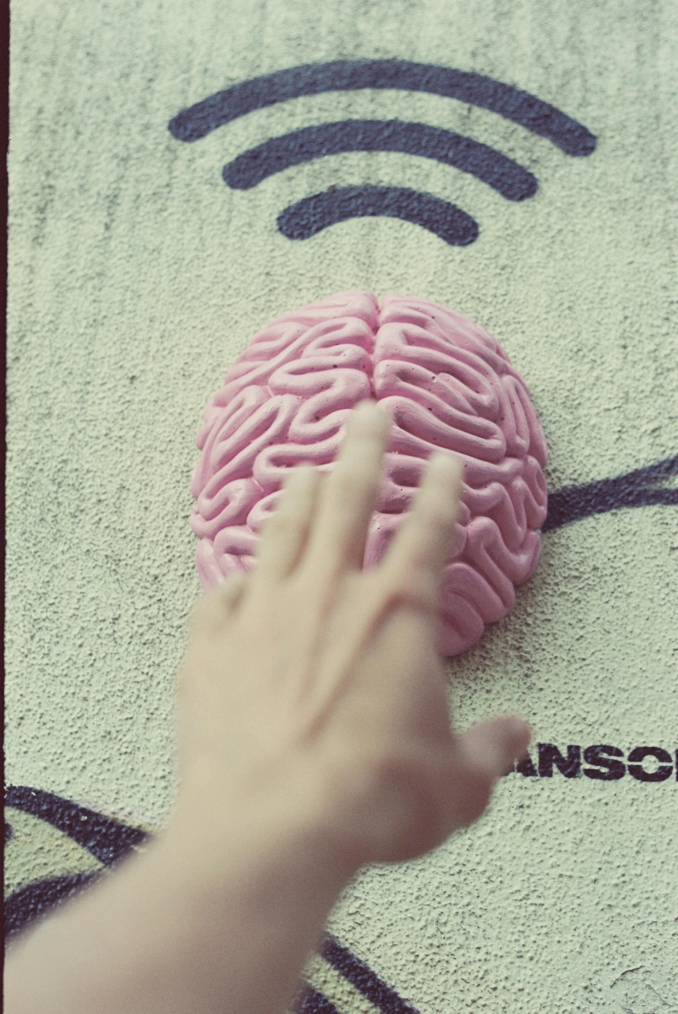 Cognitive Analytica image of a hand reaching toward a brain with a Wi-Fi symbol, representing online and in-person therapy options in Lebanon designed for accessibility and connection.