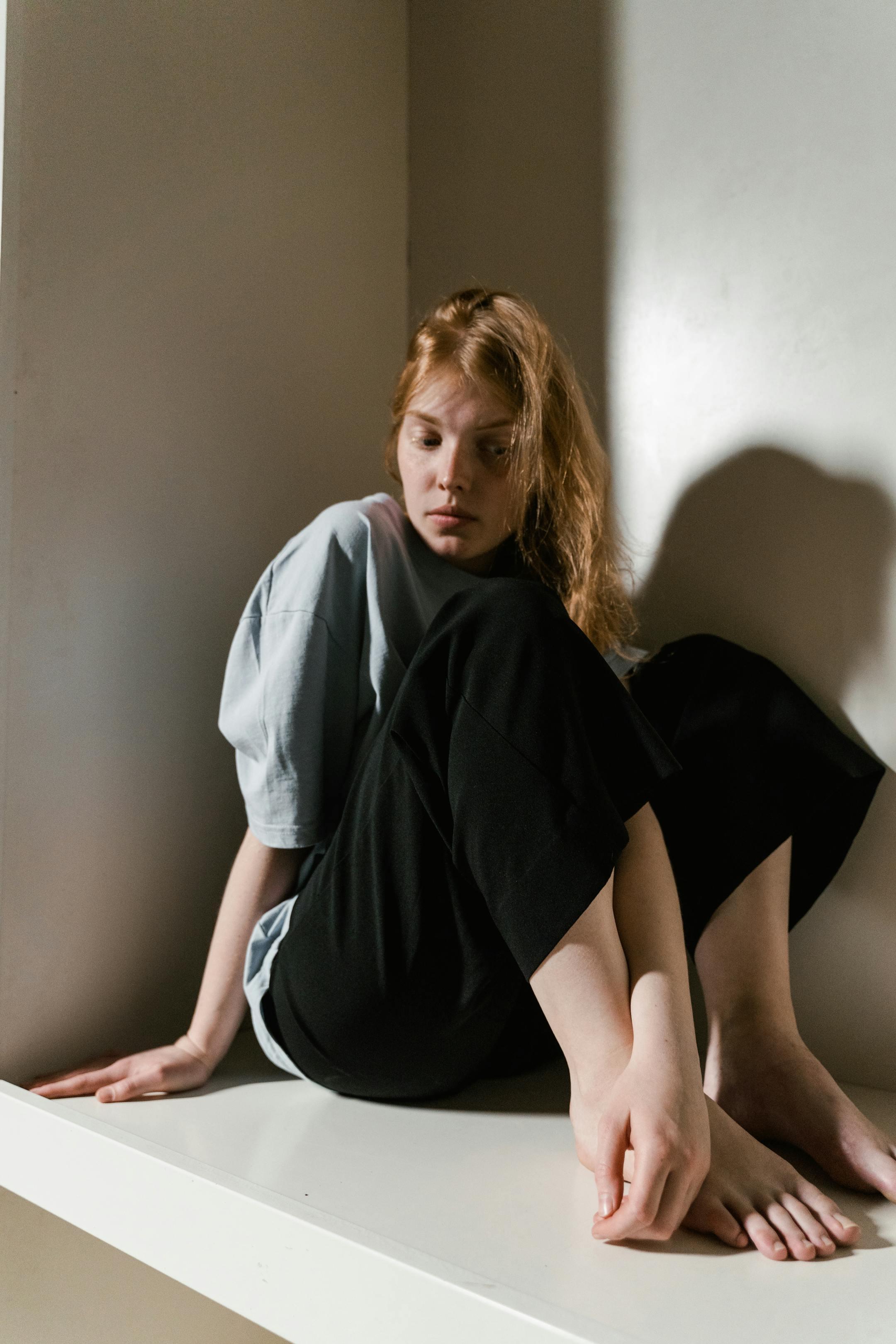 A young woman sits in a corner, deep in thought, reflecting on her emotions.