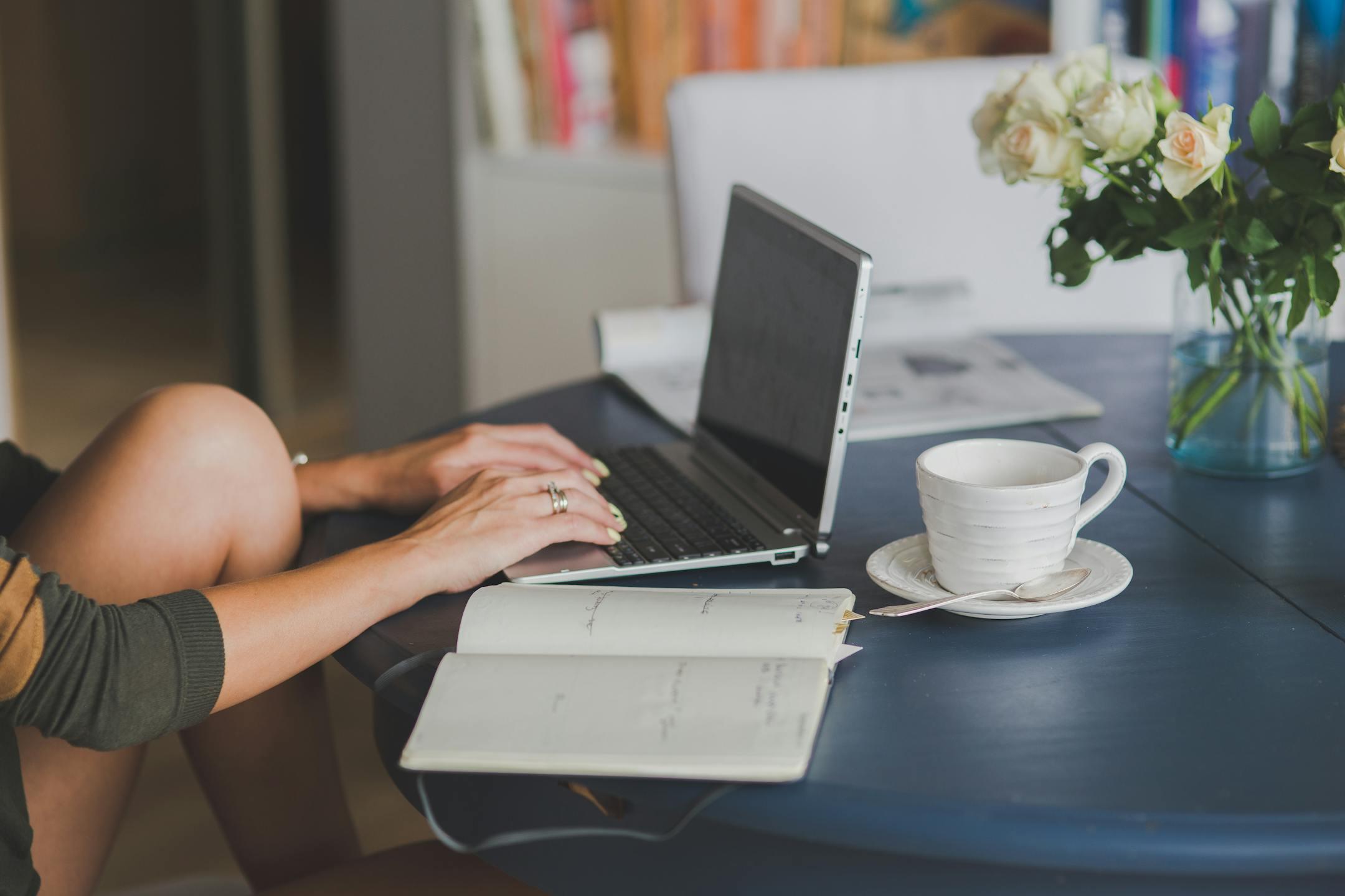 Female freelancer using a laptop with coffee, roses, and a planner on her desk, symbolizing work-life balance and mental wellness supported by Cognitive Analytica’s therapy in Lebanon