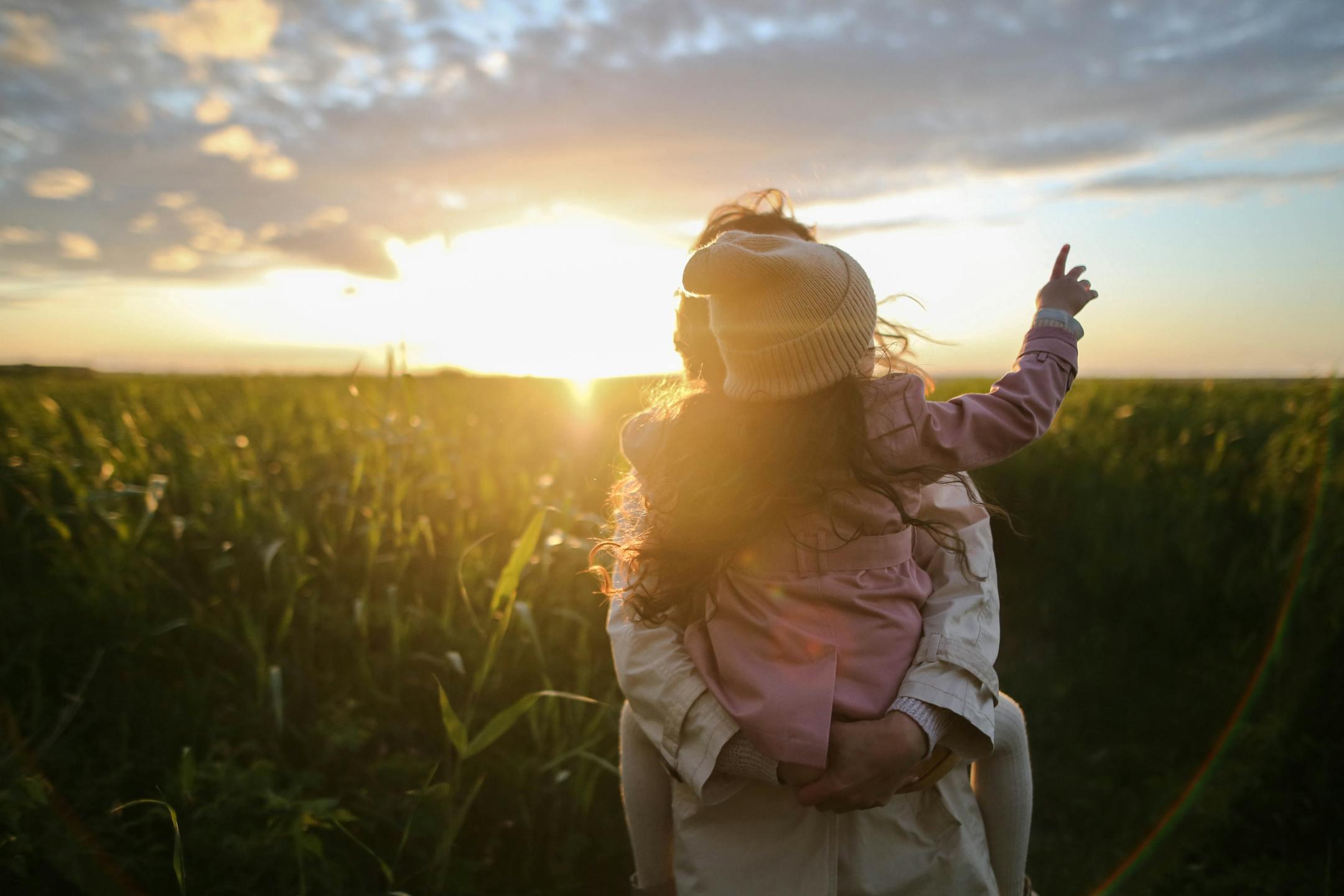 A mother and daughter embrace while pointing at the sunset in a grassy field—Cognitive Analytica family therapy in Lebanon symbolizing love, connection, and emotional healing.