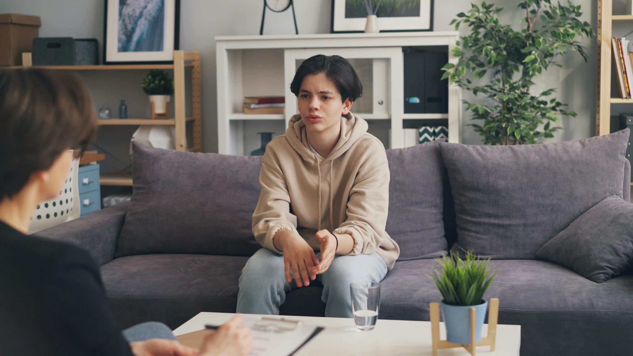 Teenager attending therapy session in a modern office, expressing emotions.