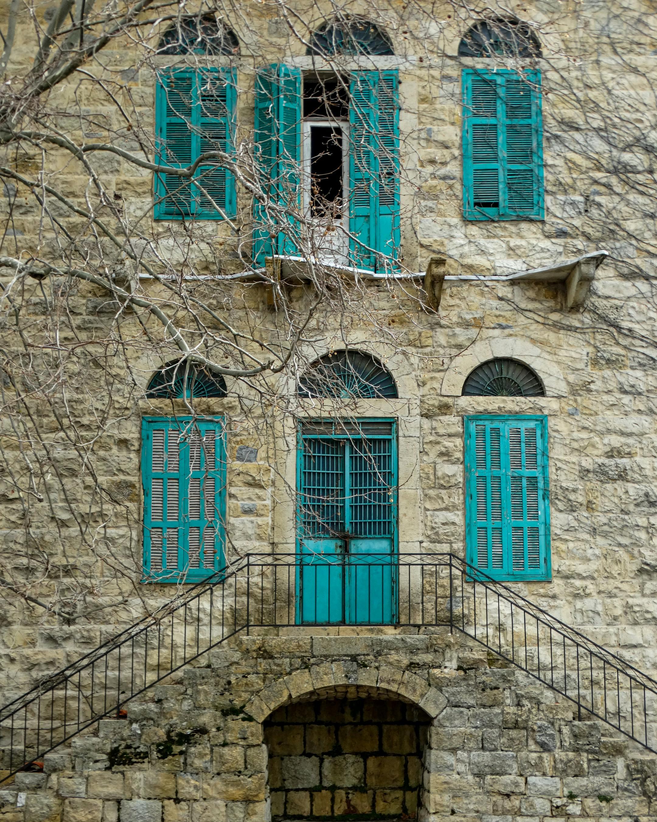 Classic Lebanese stone building with blue shutters and arched windows, showcasing rich cultural architecture.