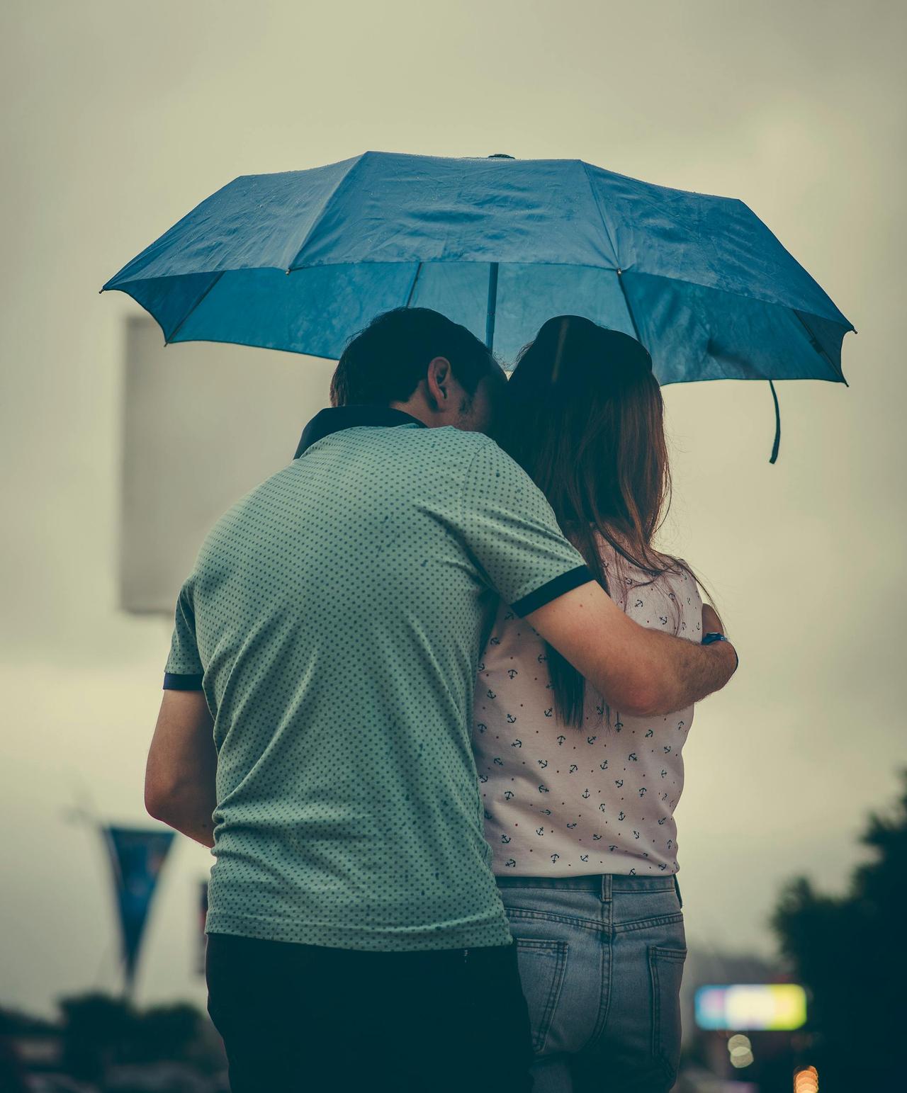 A couple embraces under a blue umbrella in a rainy street scene, evoking love, warmth, and emotional connection — symbolizing couples therapy in Lebanon with Cognitive Analytica.