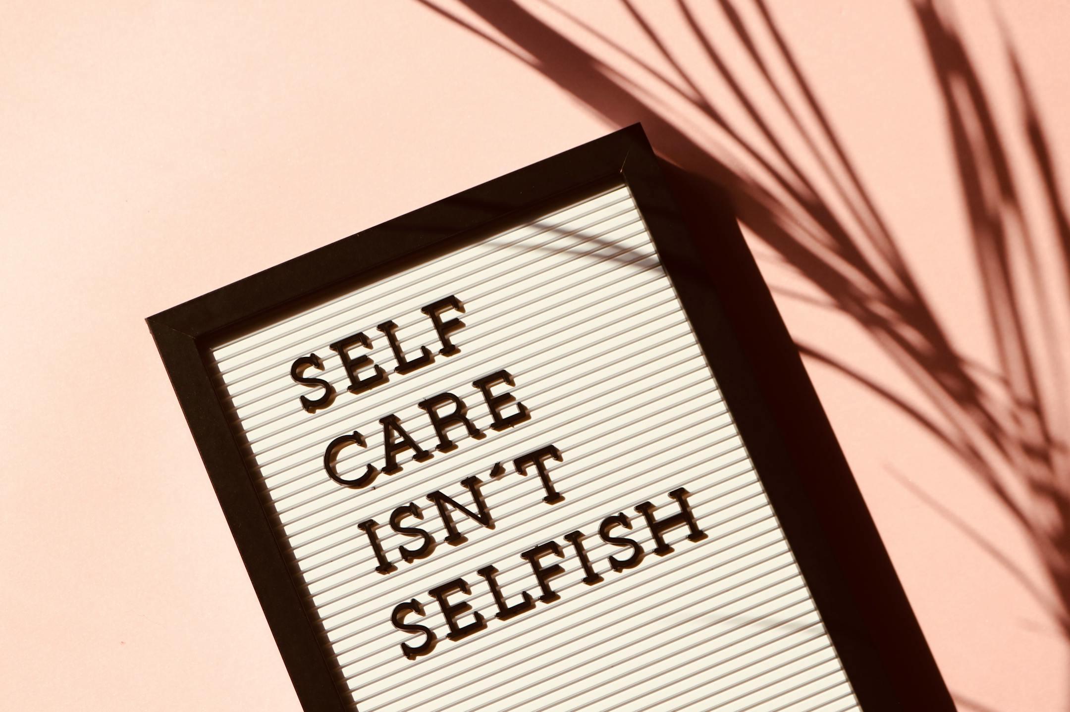 Letter board displaying the phrase <em>“Self Care Isn’t Selfish”</em> with an artistic shadow on a pink background, symbolizing Cognitive Analytica’s message of compassion and self-awareness in mental health care across Lebanon.