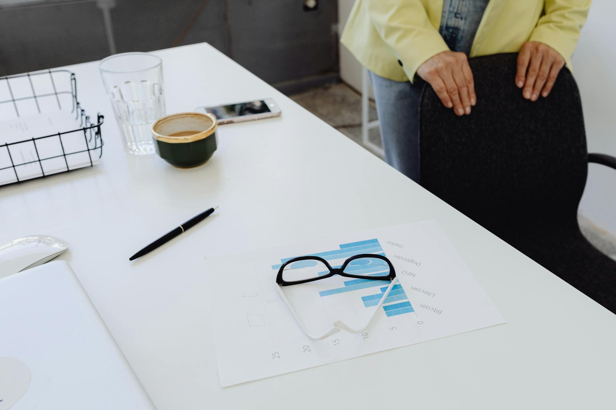 A modern office desk with charts, glasses, and coffee cup. Professional workspace setting.