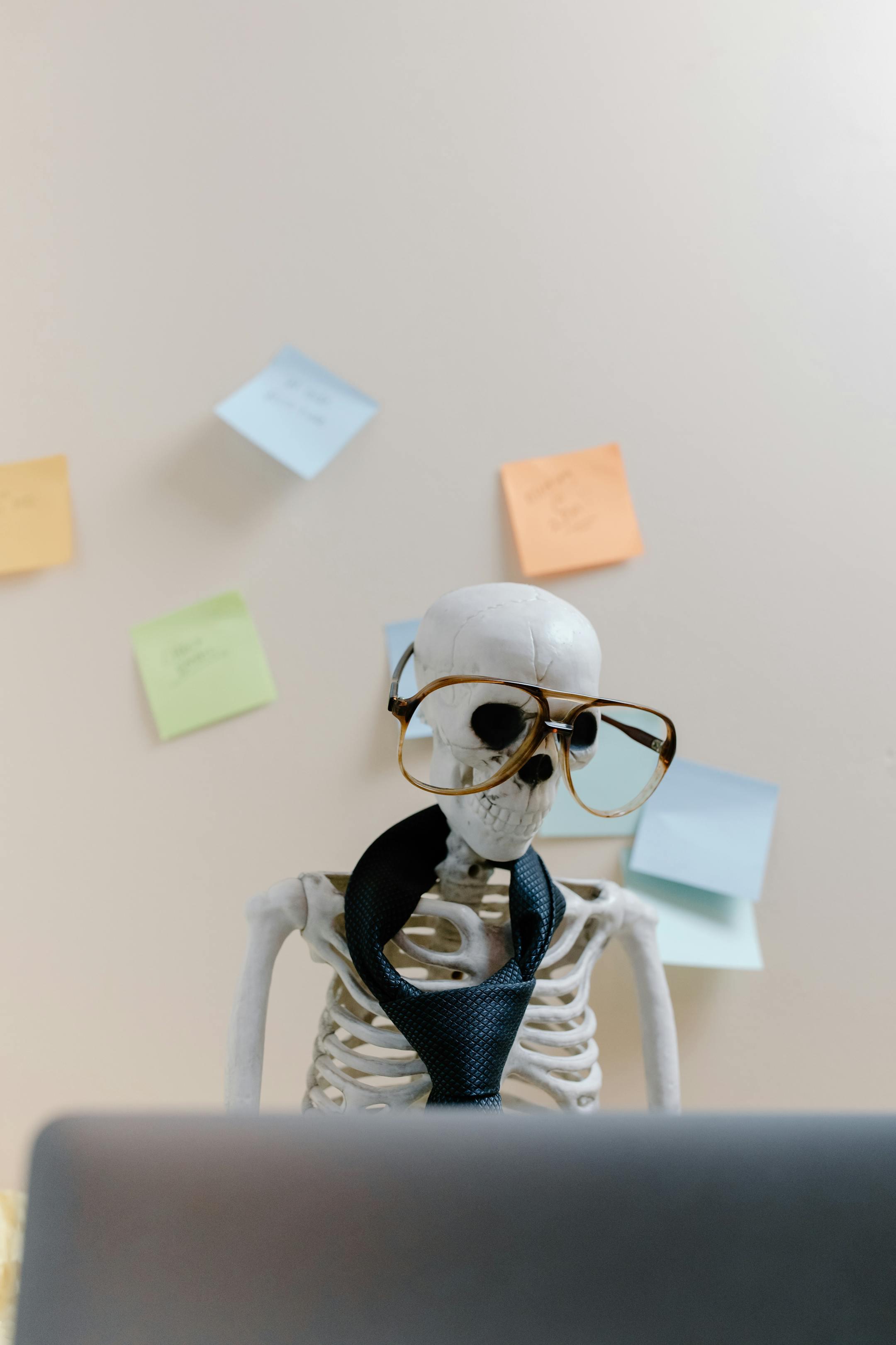 Humorous skeleton model with glasses and tie, illustrating burnout and overwork in office environment.