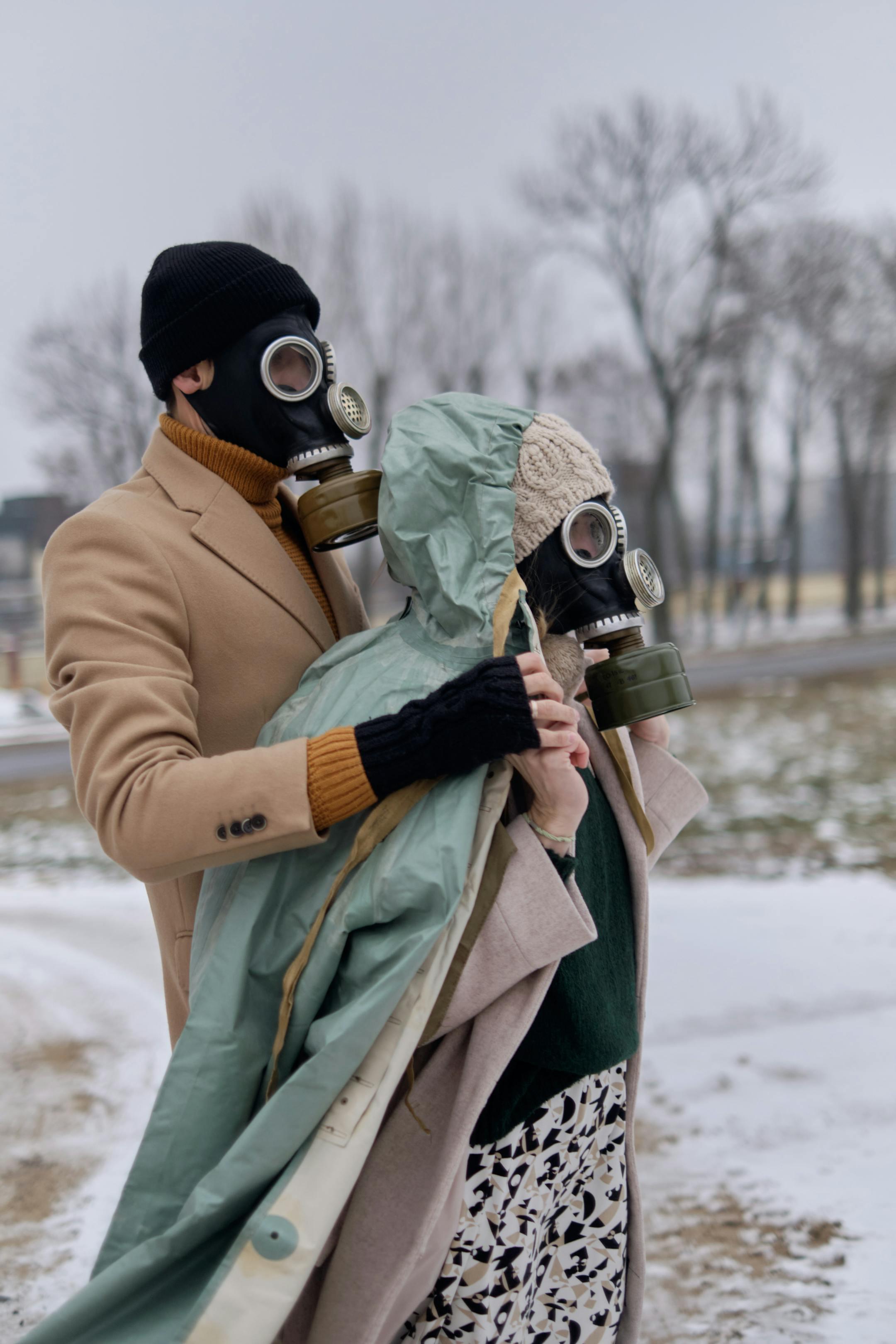 A man and a woman wearing gas masks stand outdoors shielding from pollution in winter.