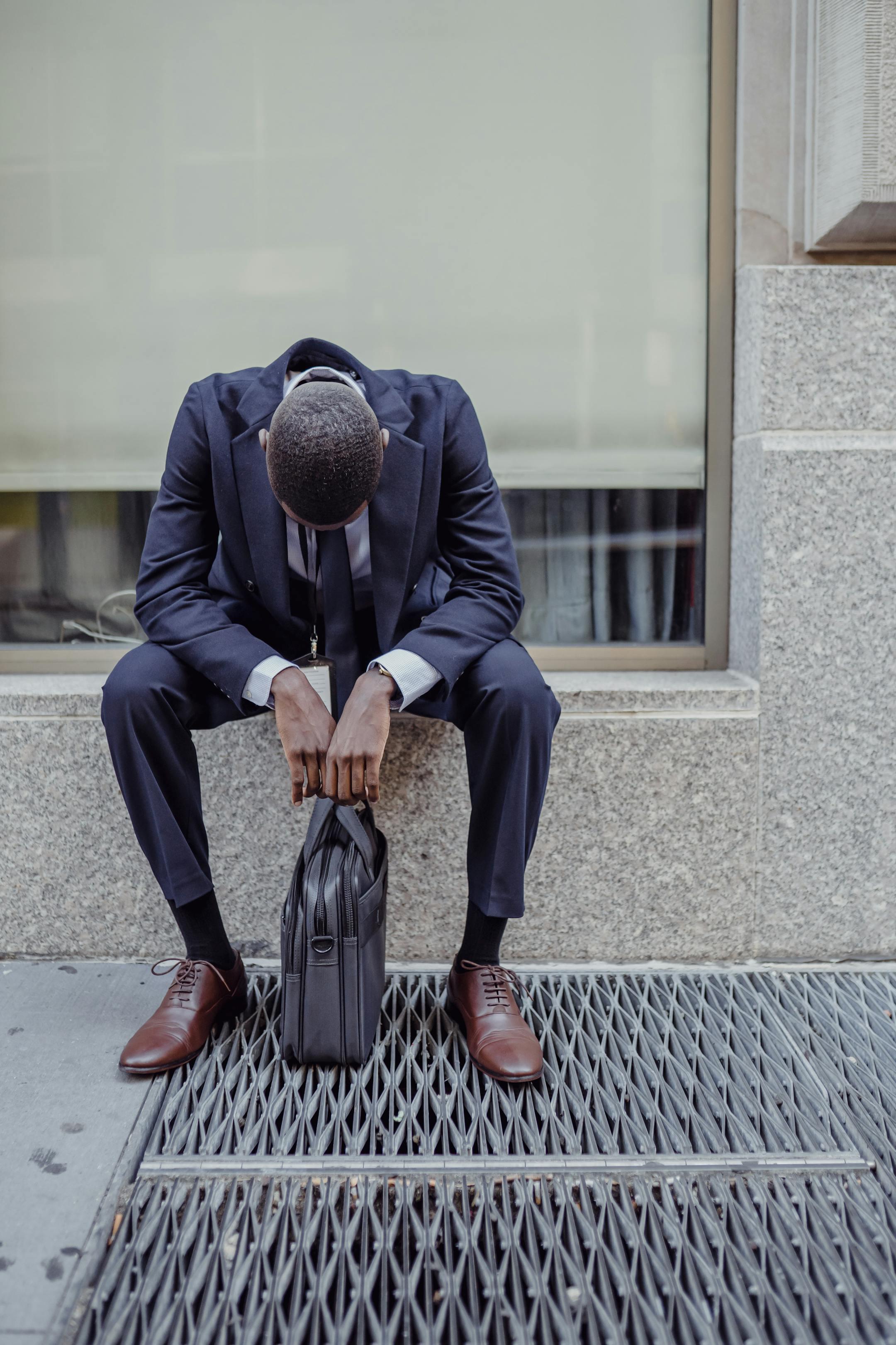 A businessman in a suit sits with his head down, expressing sadness and stress.