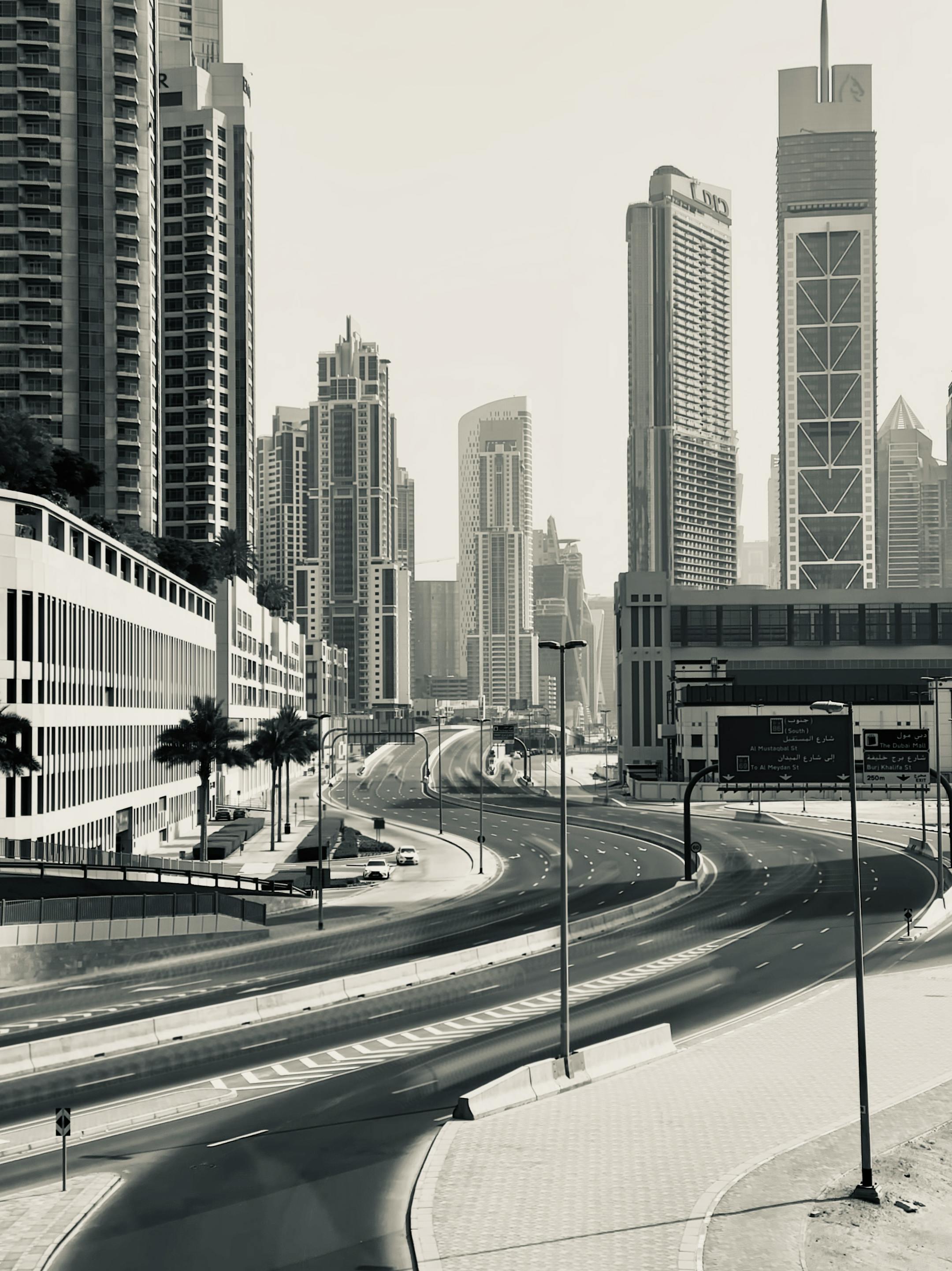 Black and white view of Dubai's iconic skyscrapers along an empty highway in daylight.
