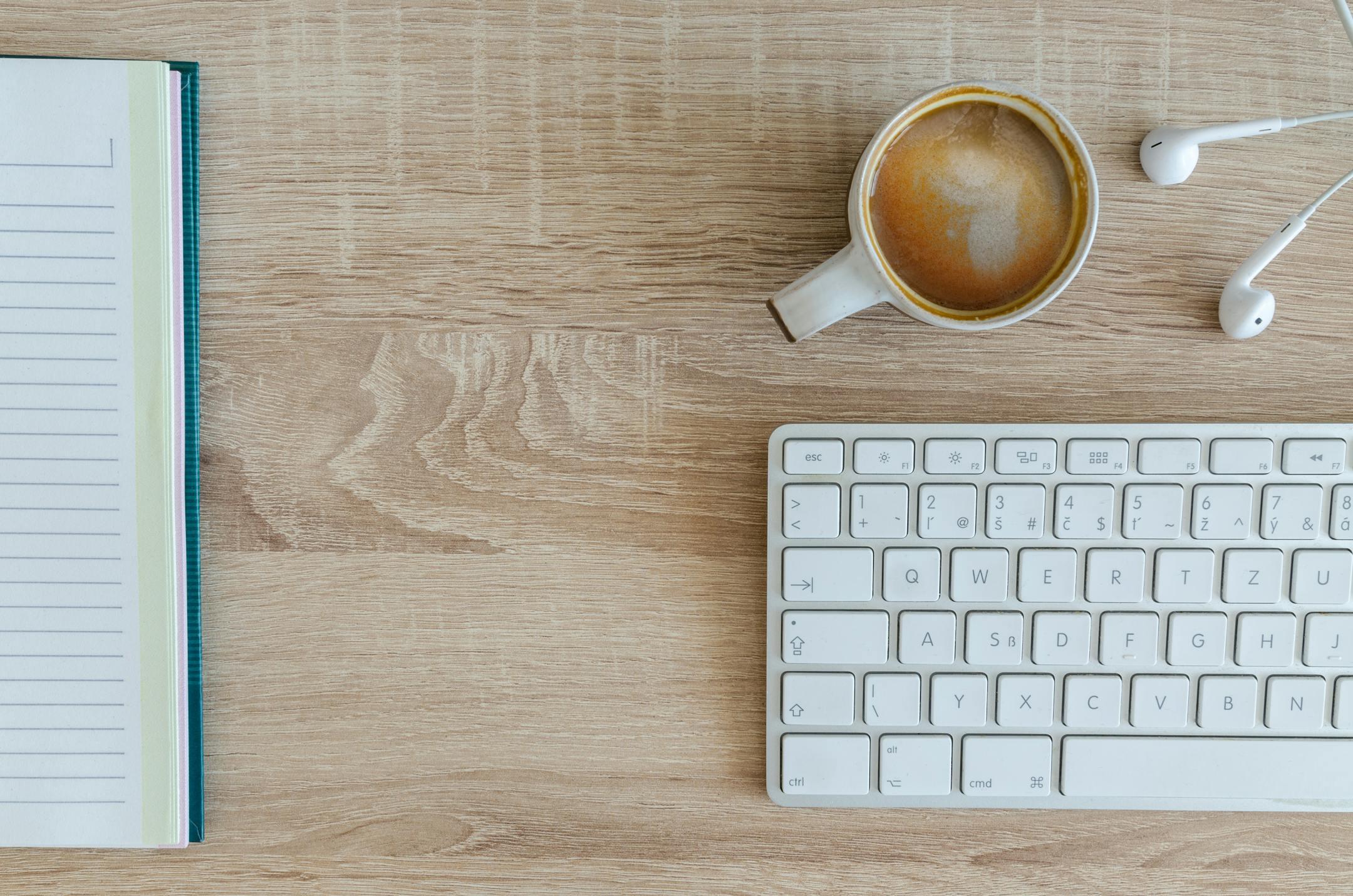 Flat lay of a workspace featuring a cup of coffee, keyboard, and notebook on a wooden desk — symbolizing Cognitive Analytica’s organized, evidence-based, and ethical approach to quality mental health care in Lebanon.