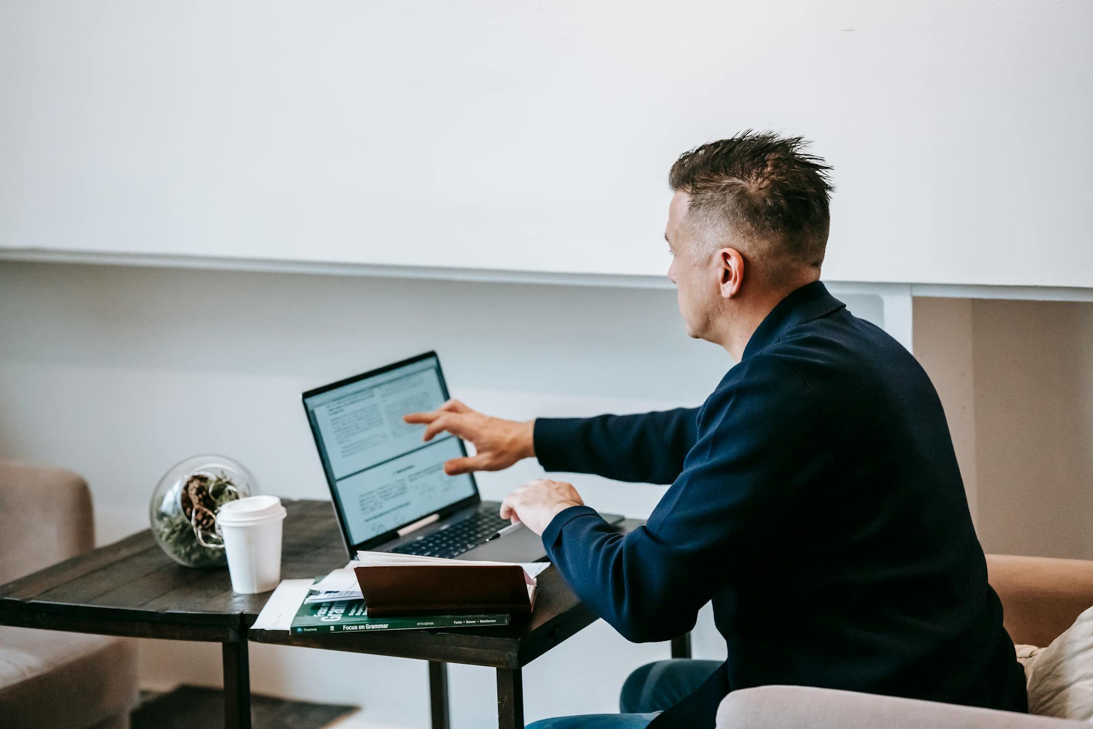 Man working remotely on a laptop in a cozy home office setting with coffee and documents.