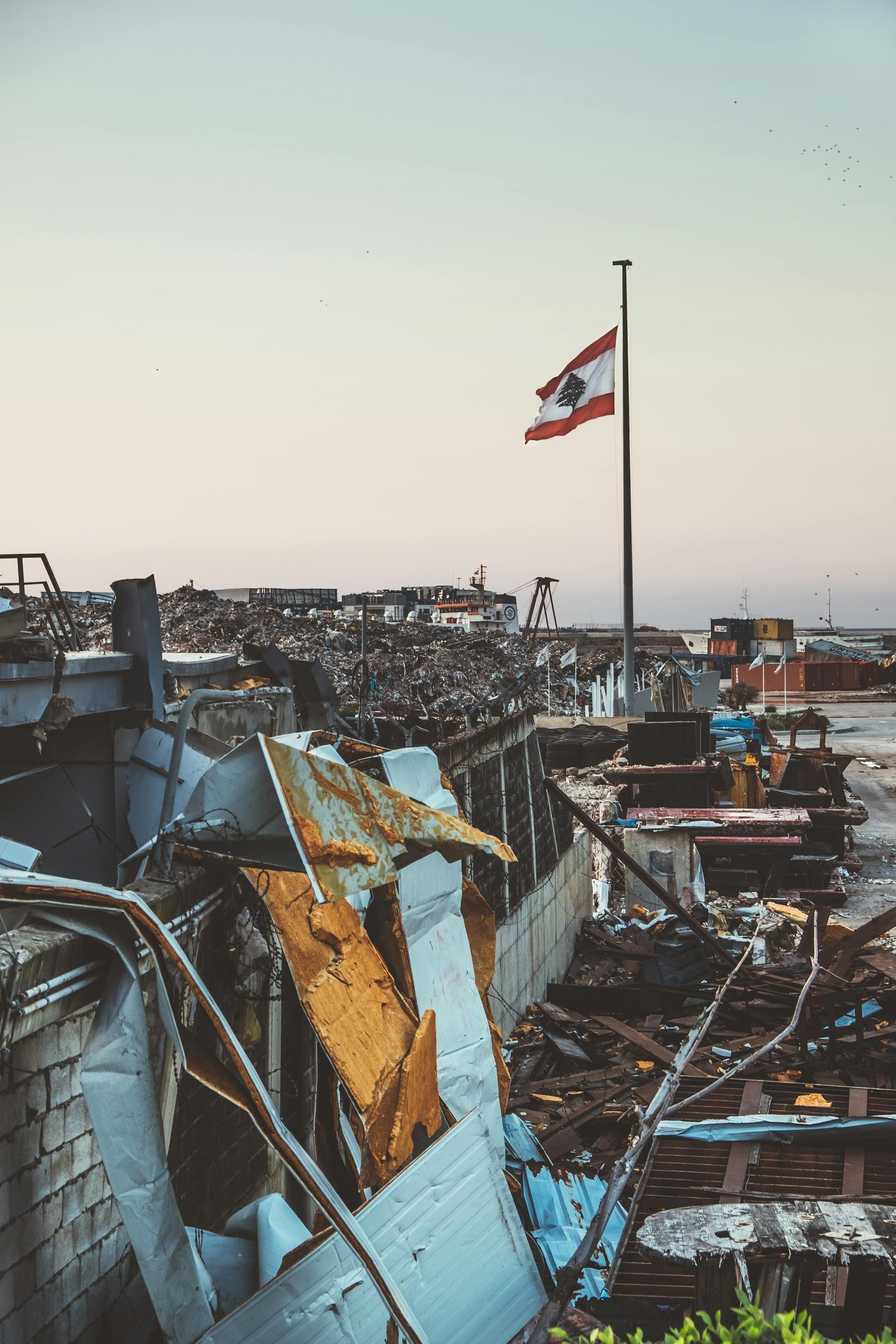 Debris and destruction at Beirut harbor with Lebanese flag post-explosion scene.