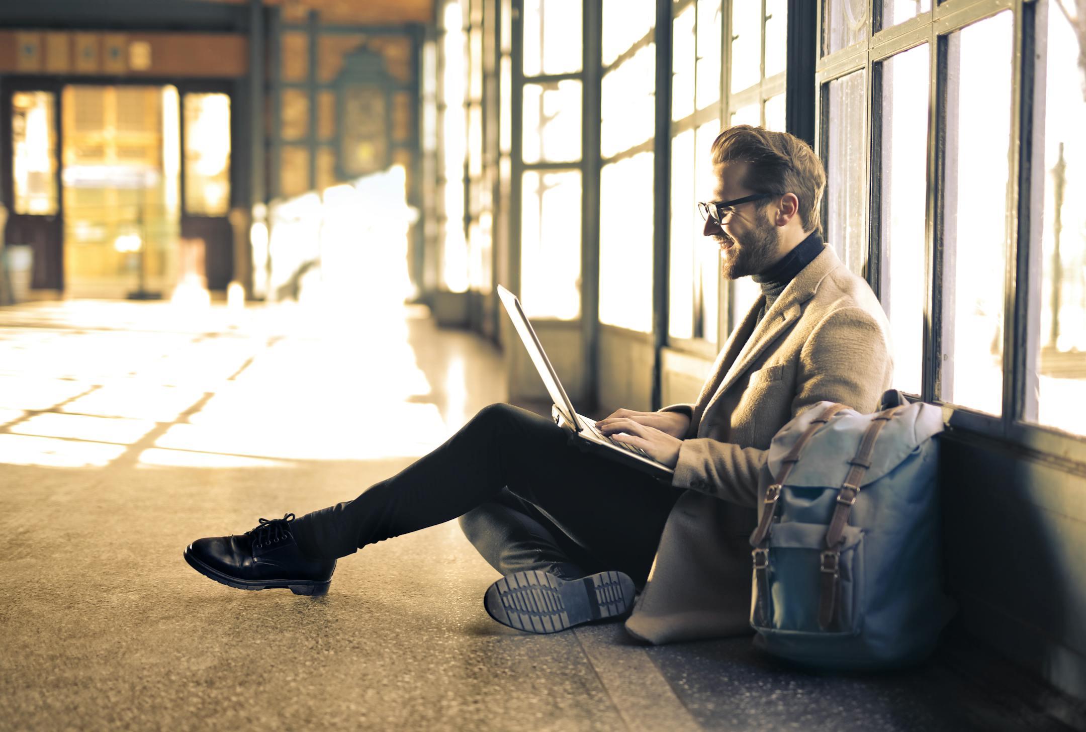 Man working on a laptop at a train station with sunlight streaming through the window, symbolizing Cognitive Analytica’s global purpose and commitment to accessible, science-based mental health support.