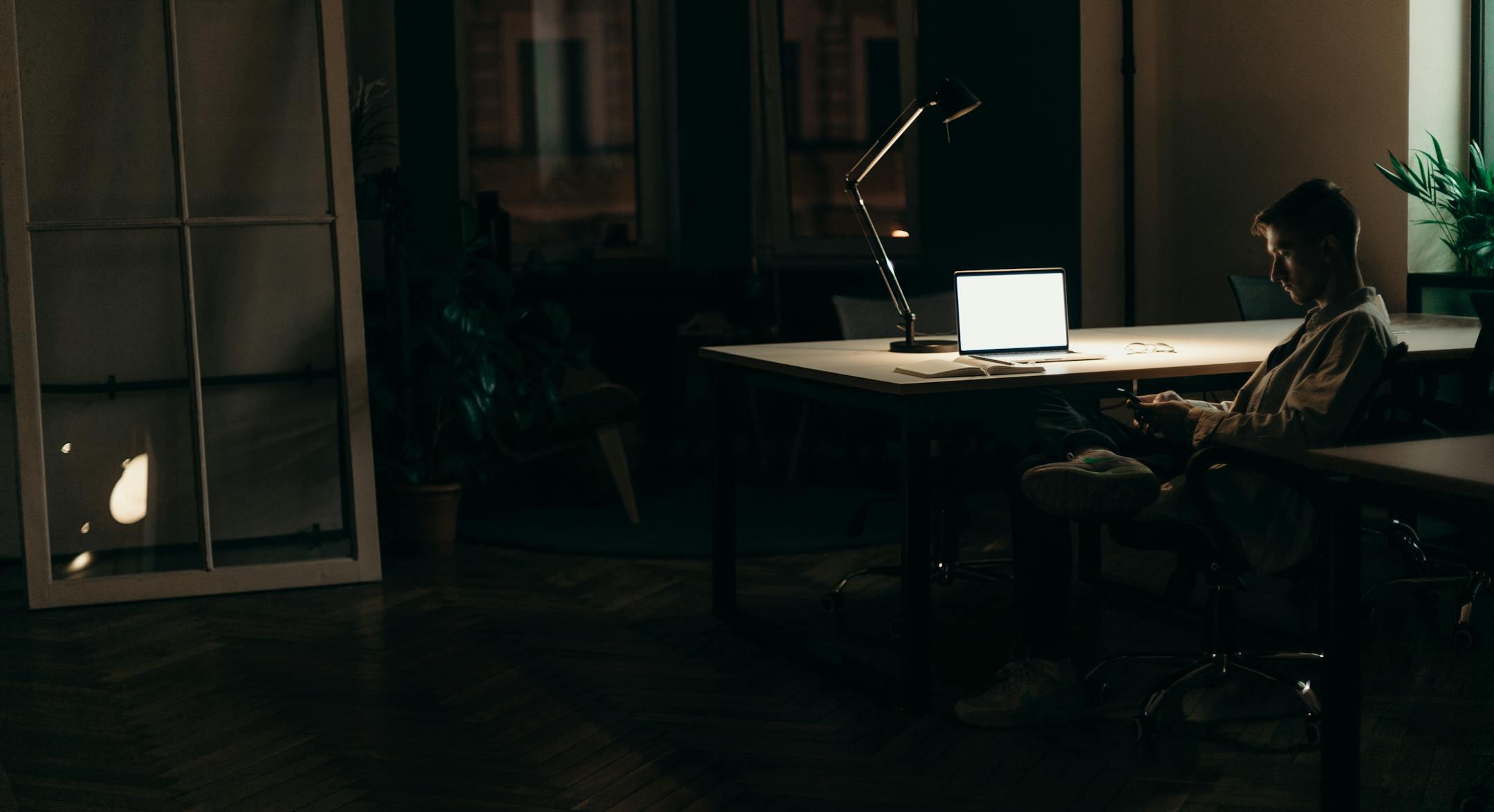 A man using his laptop in a dimly lit office at night, highlighting a dedicated work environment.