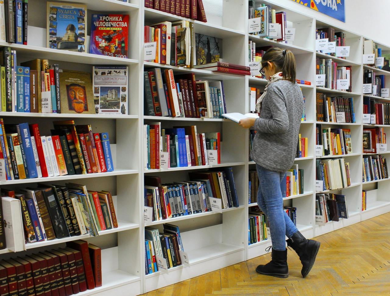 A young lebanese woman stands reading a book in a well-stocked library.