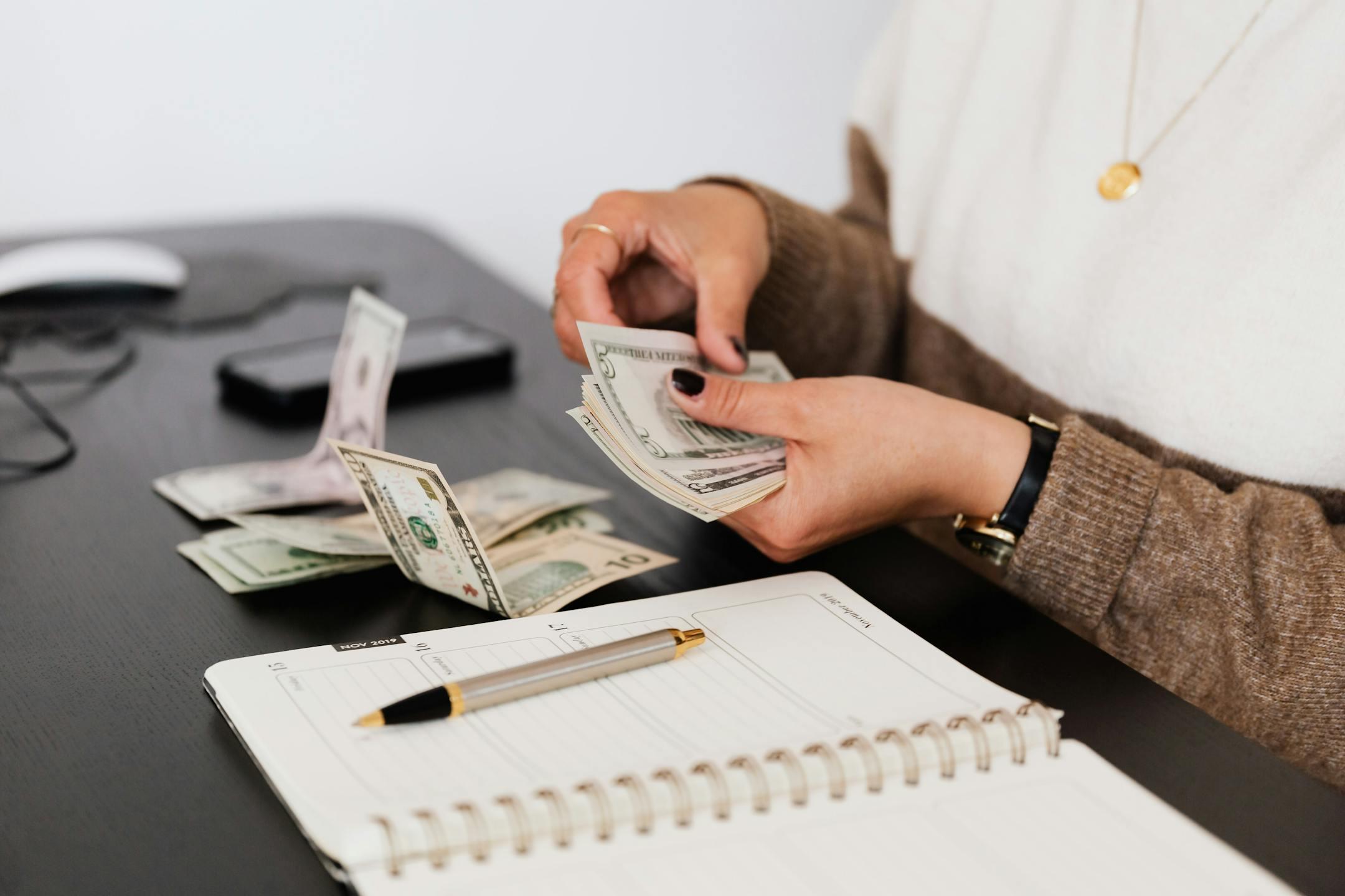 Close-up of a person counting cash beside a notepad on a desk, representing careful budgeting and financial planning for affordable therapy with Cognitive Analytica in Lebanon.