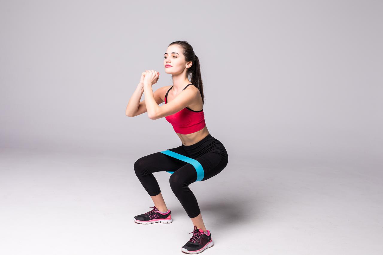 slim-woman-doing-squats-with-fitness-elastic-loop-band-isolated-white-wall.jpeg