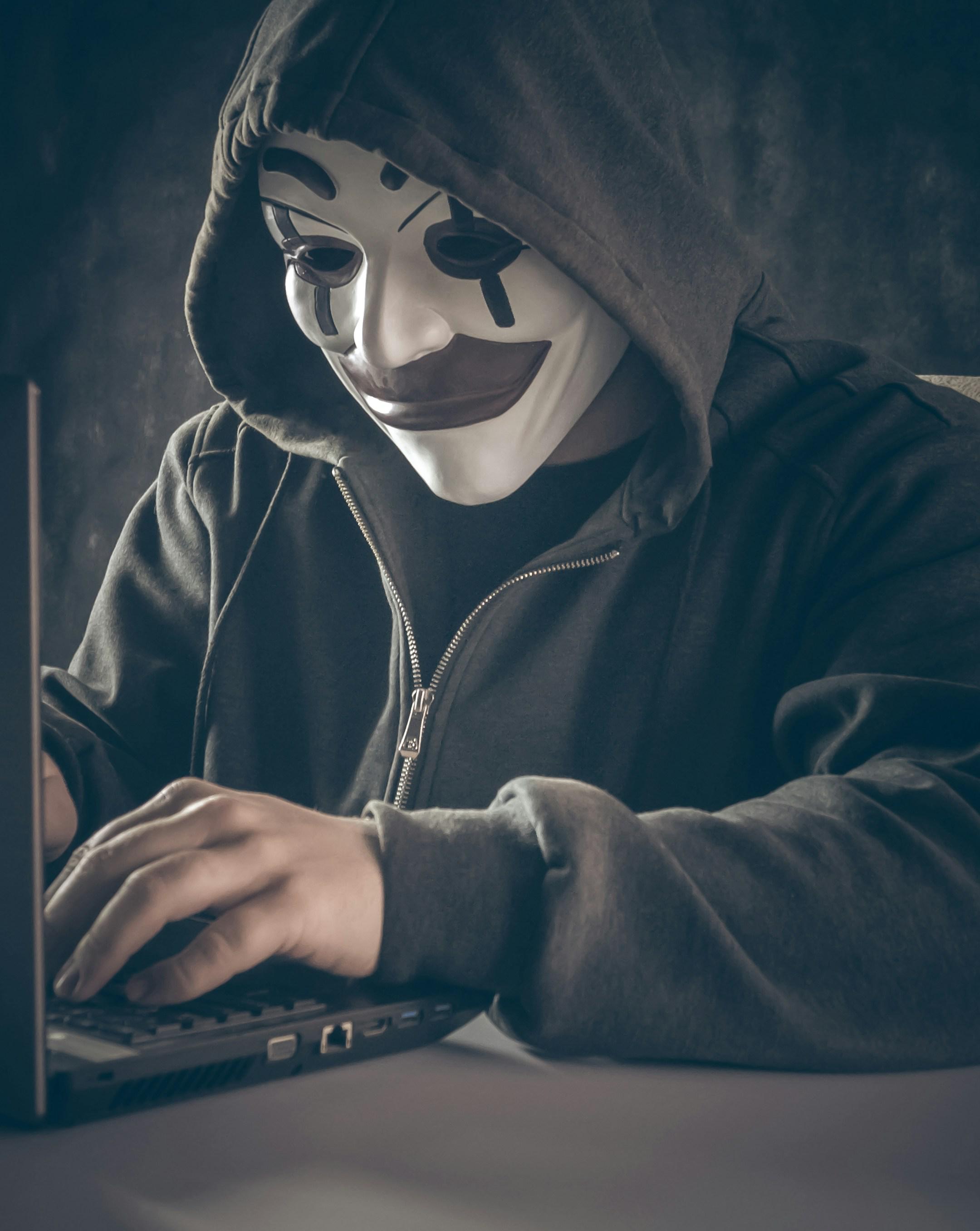 Anonymous computer hacker in white mask and hoodie. Using laptop computer for cyber attack and calling on cellphone. Special photo processing film grain, noise. Subscribe my channel: https://www.youtube.com/@earthzoom | Donation: https://fantalks.io/r/bermixstudio - any amount appreciated 🤘