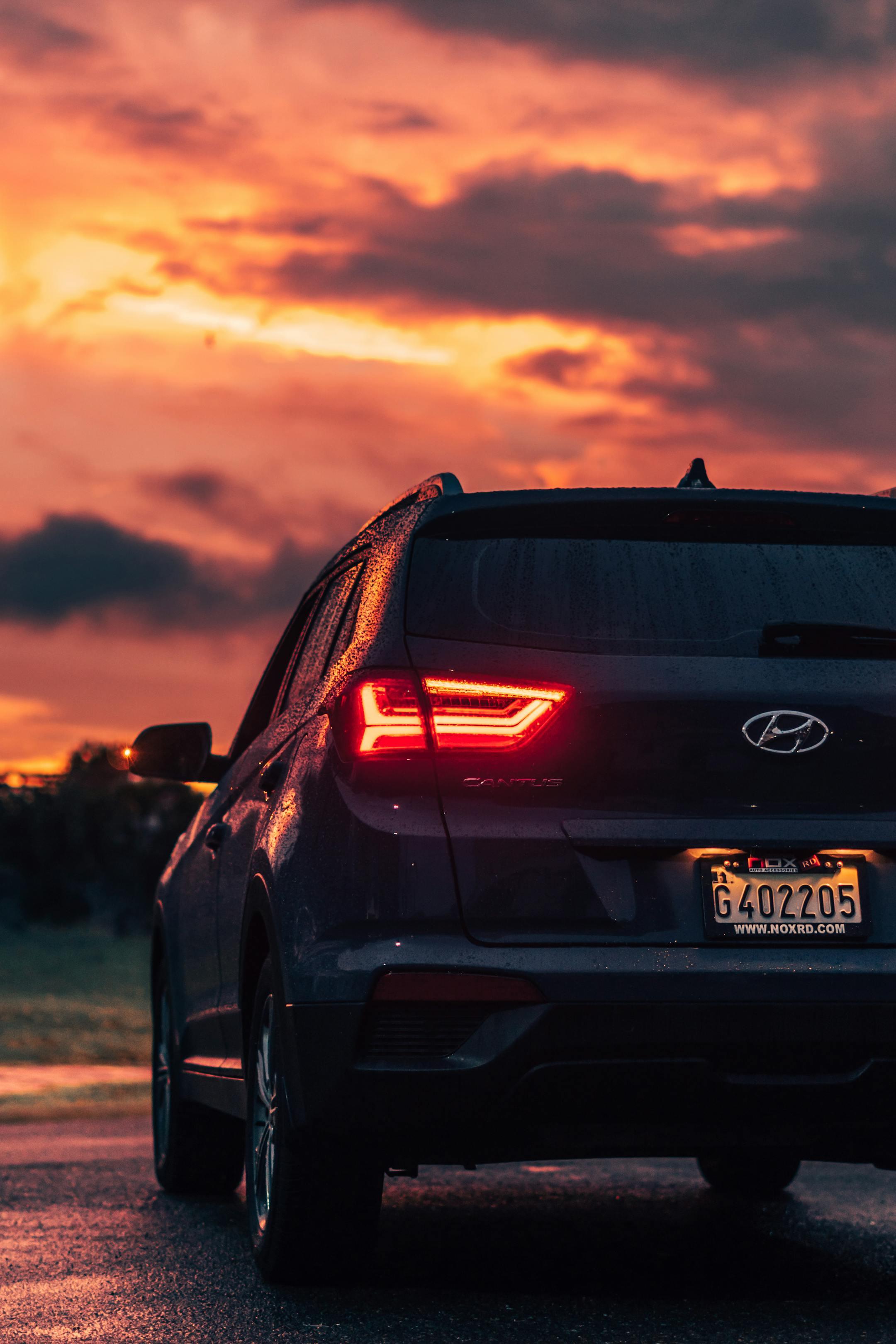 Rear view of a modern Hyundai SUV on a wet road during a vibrant sunset, showcasing dramatic cloudscape.