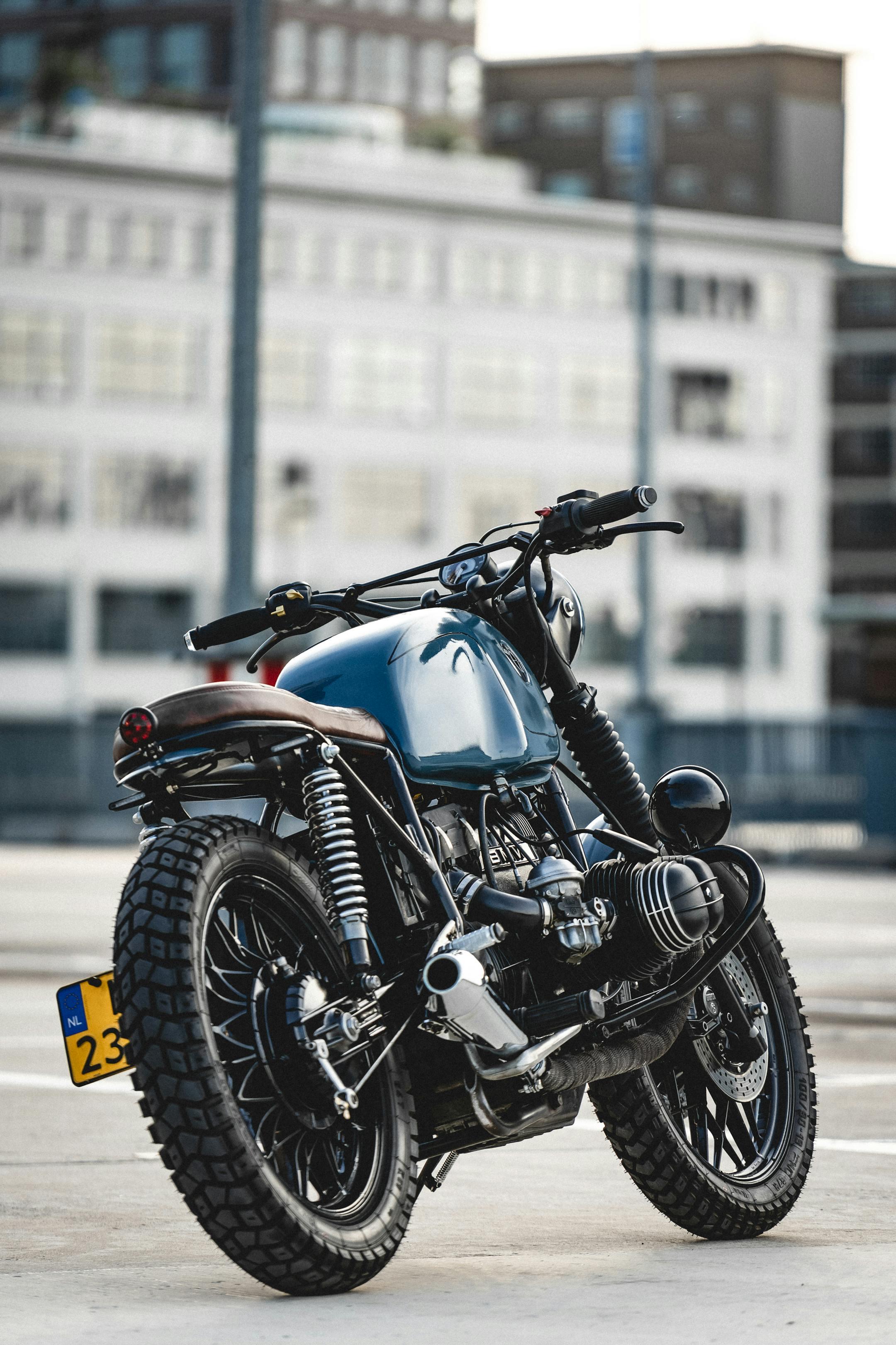 A sleek cafe racer motorcycle parked on asphalt with modern architecture in the background.