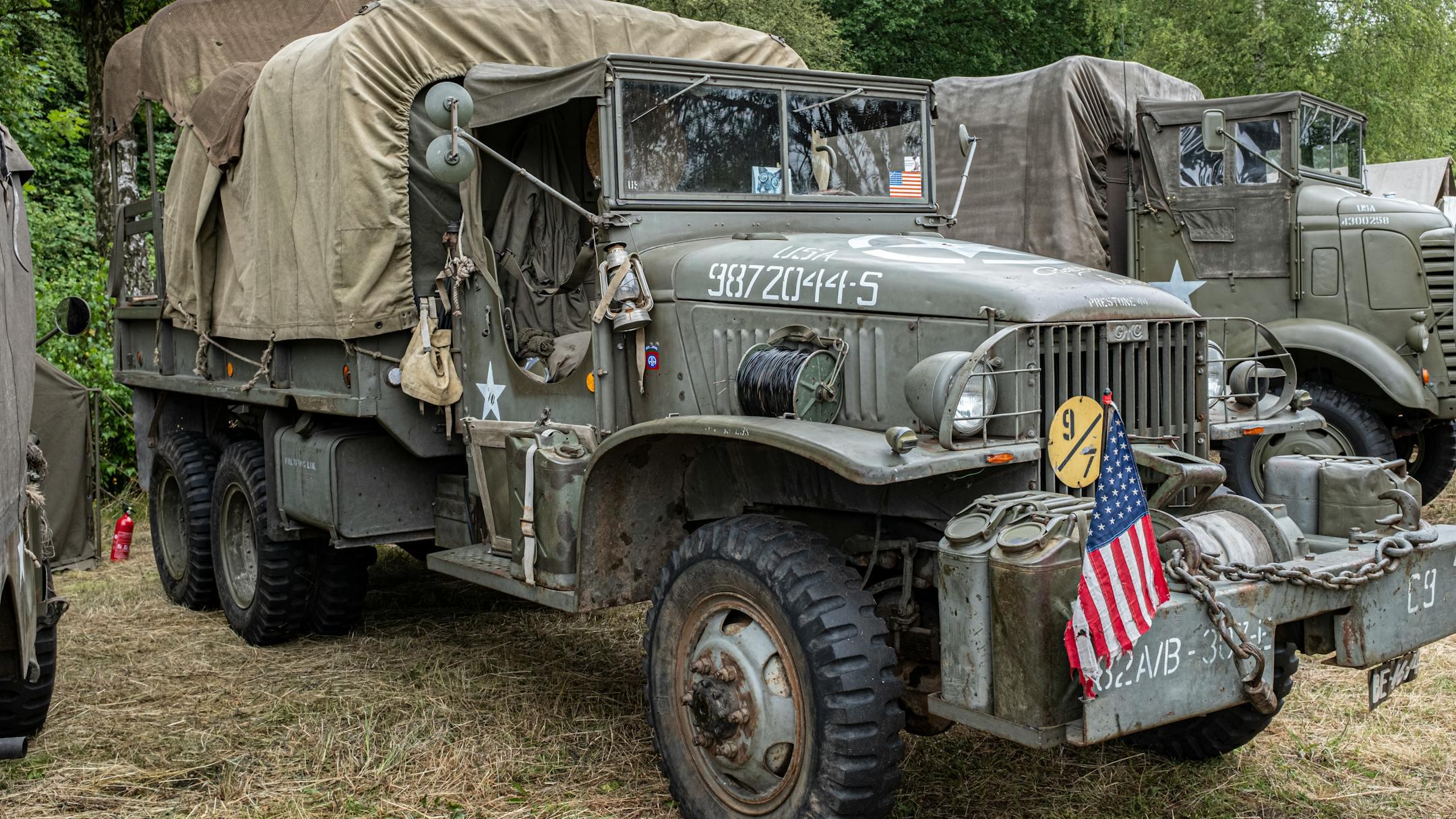 Rustic military truck parked outdoors with canvas cover and American flag.