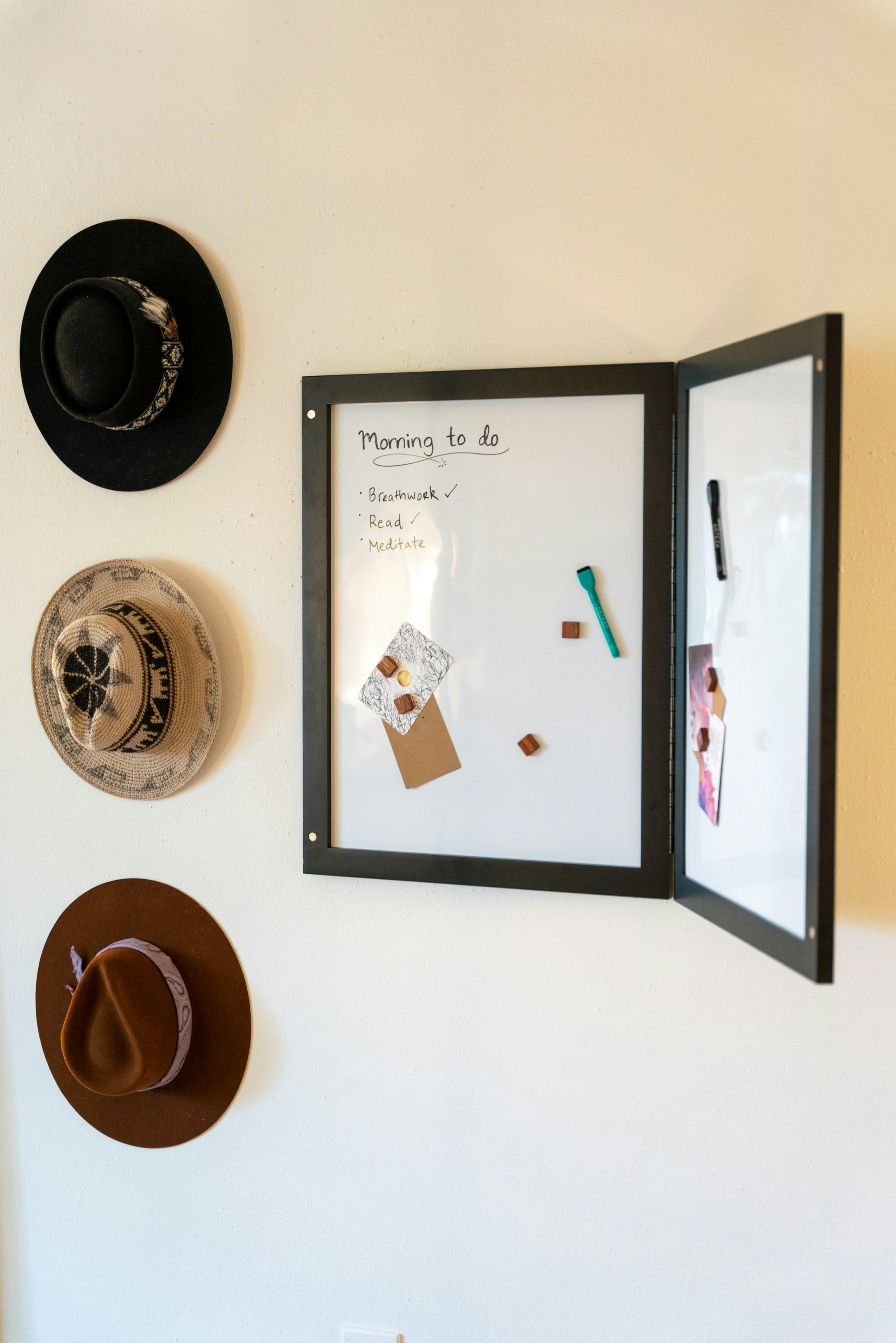 A secret whiteboard displays a morning to-do list, including breathwork, reading, and meditation. It's adorned with hanging hats, offering a practical and mindful start to the day.