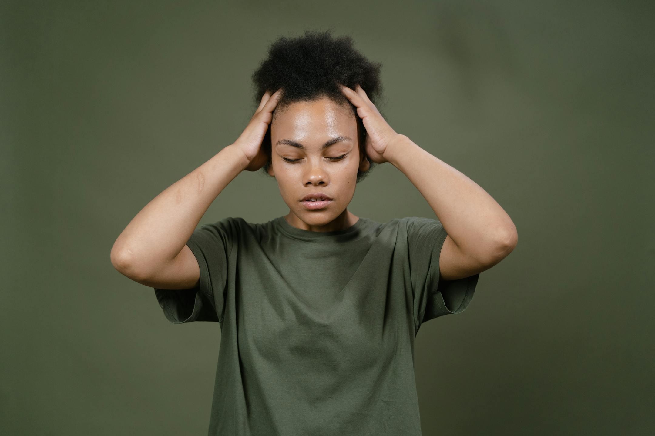 Portrait of a woman with afro hair holding her head, depicting stress or headache.
