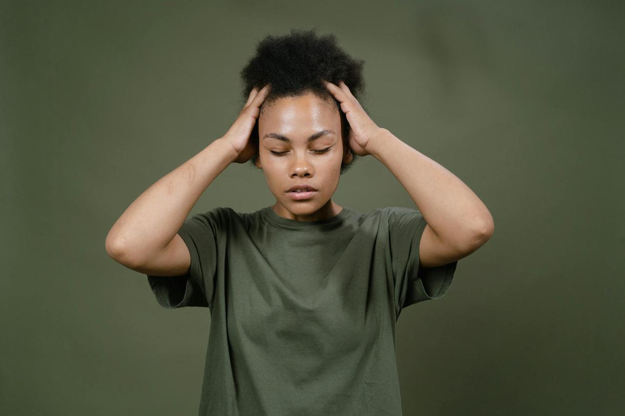 Portrait of a woman with afro hair holding her head, depicting stress or headache.