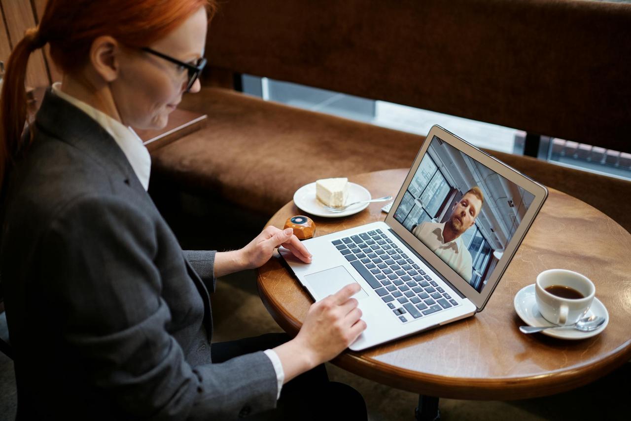 Business woman engaged in a video call meeting in a cozy cafe setting, using a laptop.