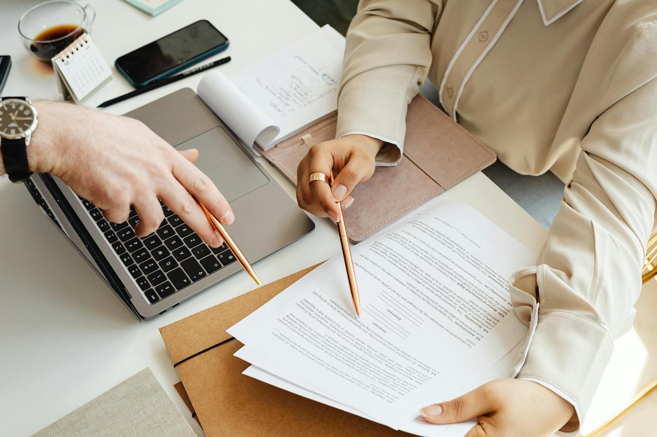 Office teamwork with two people reviewing documents and using a laptop