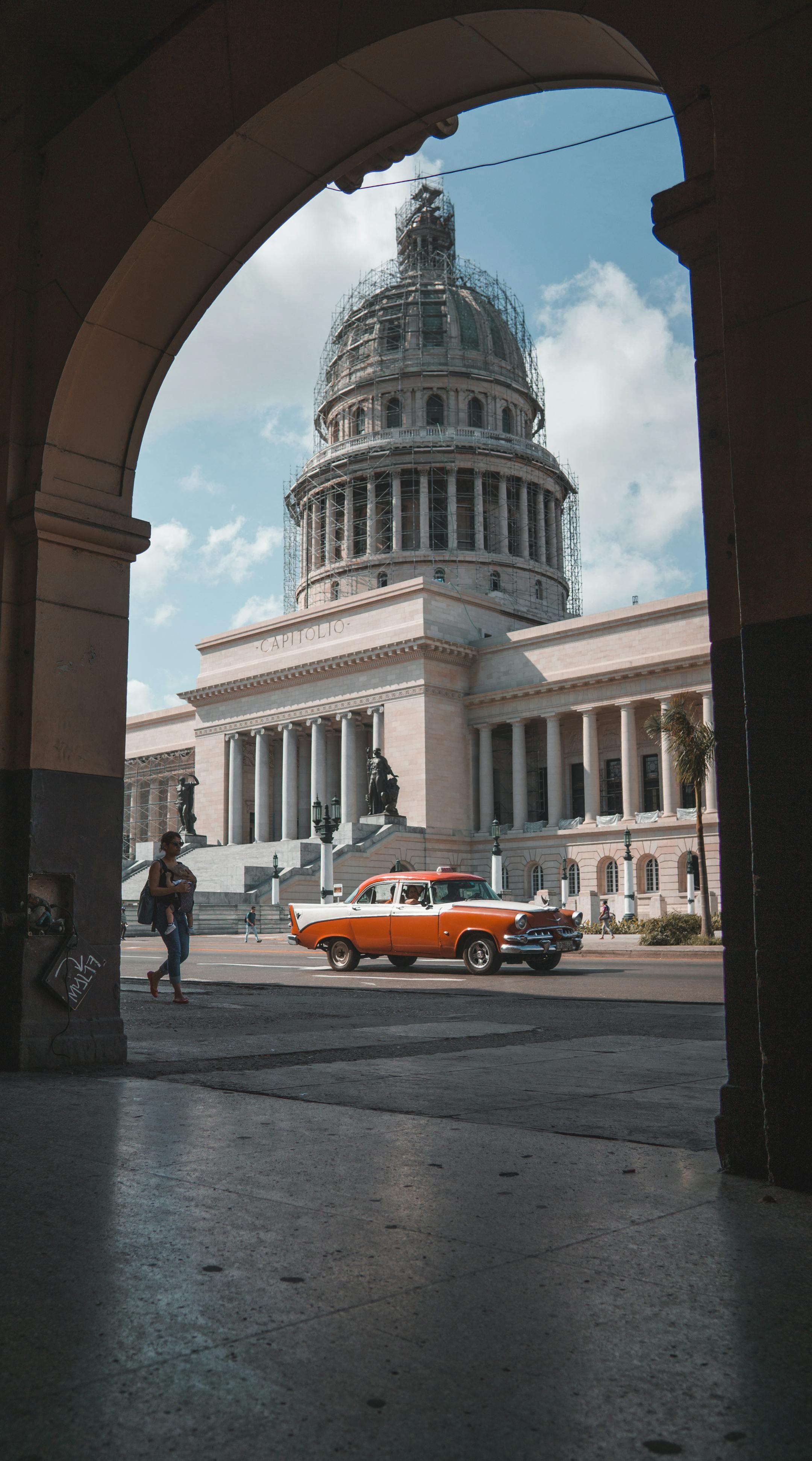 Vintage car passing by the Capitol Building in Havana, Cuba, under a sunny sky.