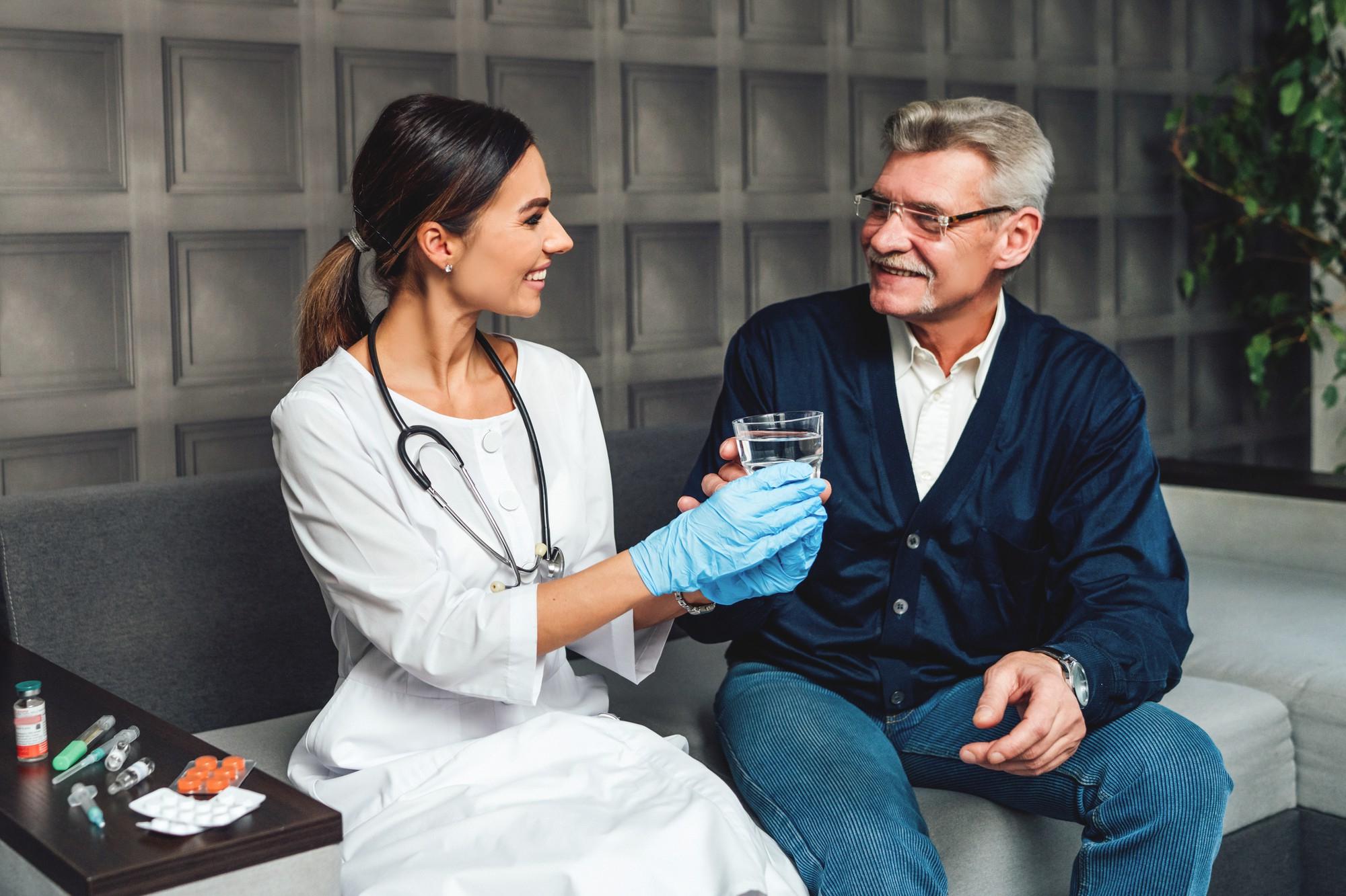 A doctor handing a glass of water to an elderly man