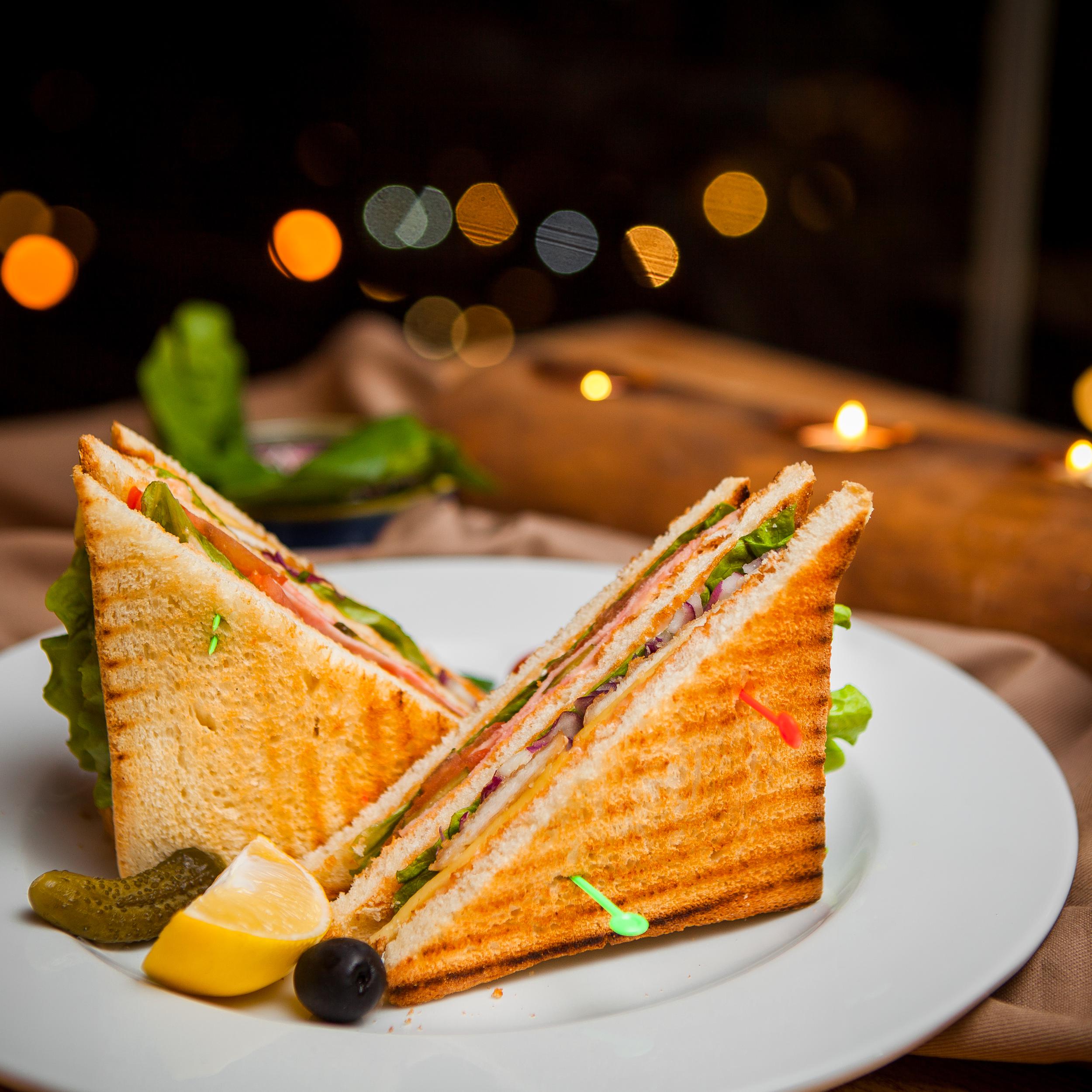 side-view-club-sandwich-with-salted-cucumbers-lemon-olives-round-white-plate.jpg