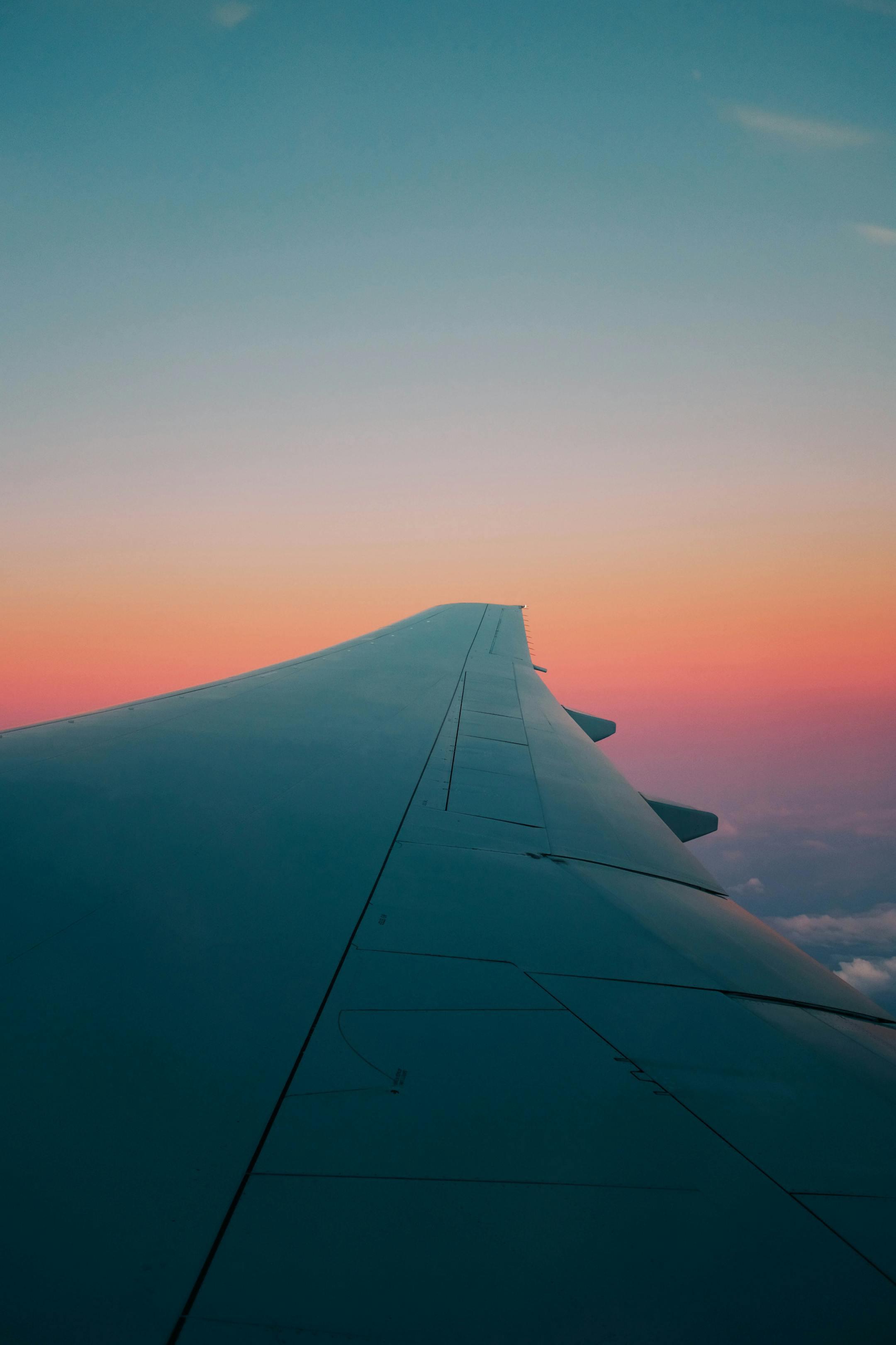 View of an airplane wing against a colorful sunrise sky, highlighting aviation and travel.
