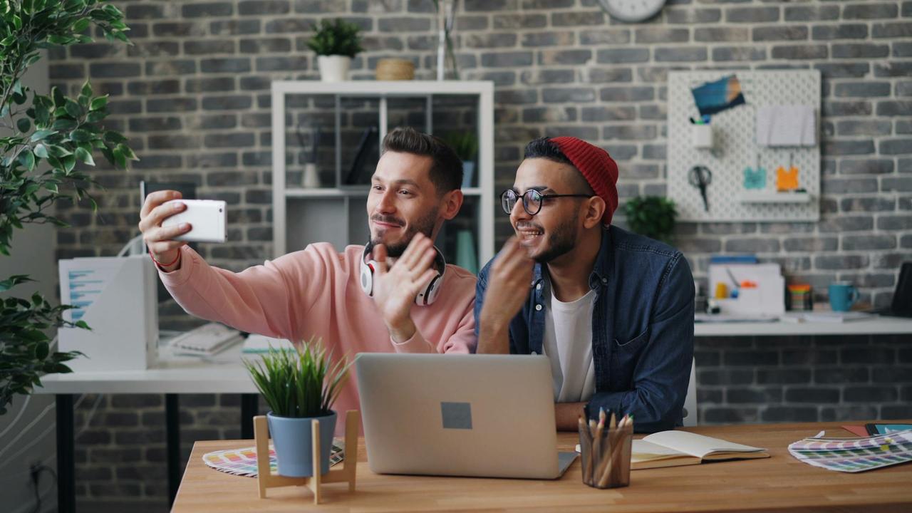 Two young men smiling and taking a selfie in a modern, creative office space.