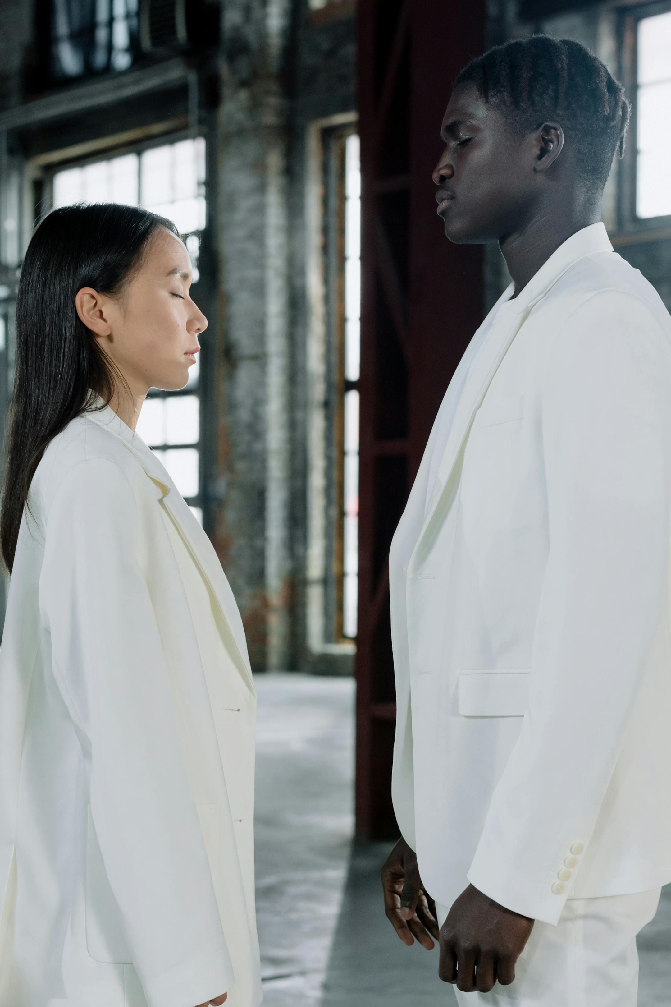 Side view of two diverse professionals in white suits facing each other indoors.