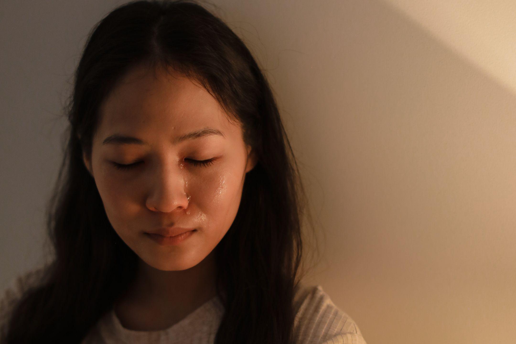 A woman with closed eyes and tears on her face, highlighting emotions of sadness indoors.
